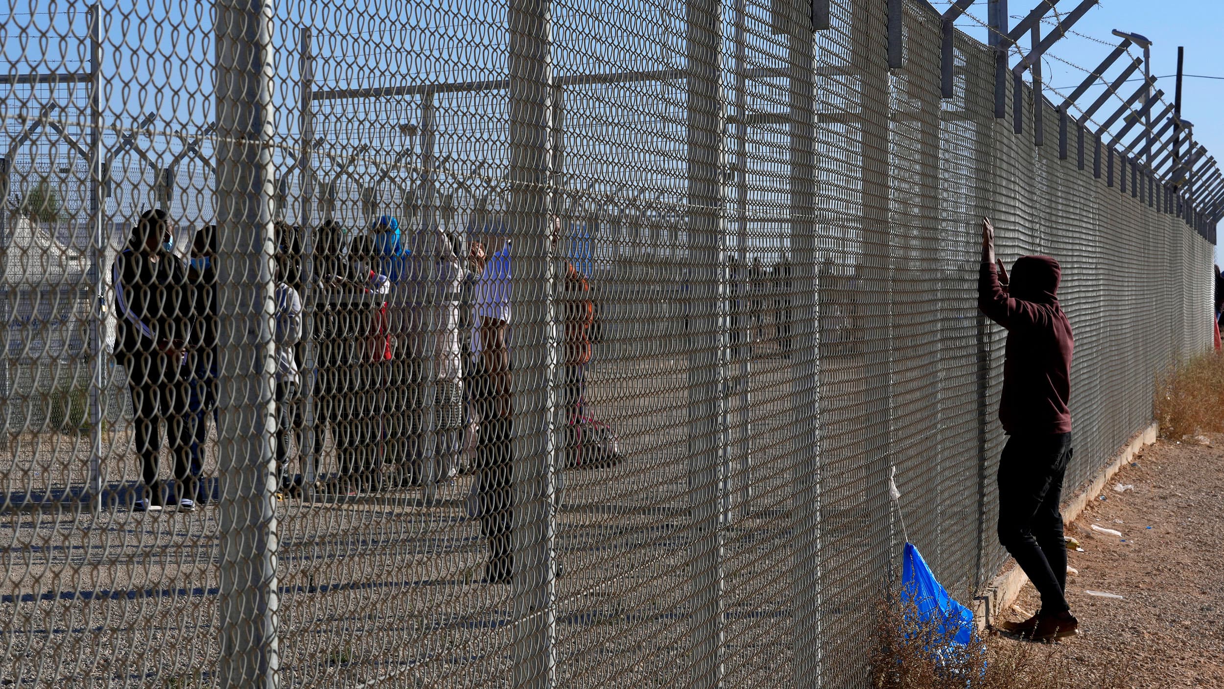A migrant looks through a fence as others wait in a line to be registered inside a refugee camp in Kokkinotrimithia, outside Nicosia, Cyprus, Tuesday, Nov. 9, 2021.