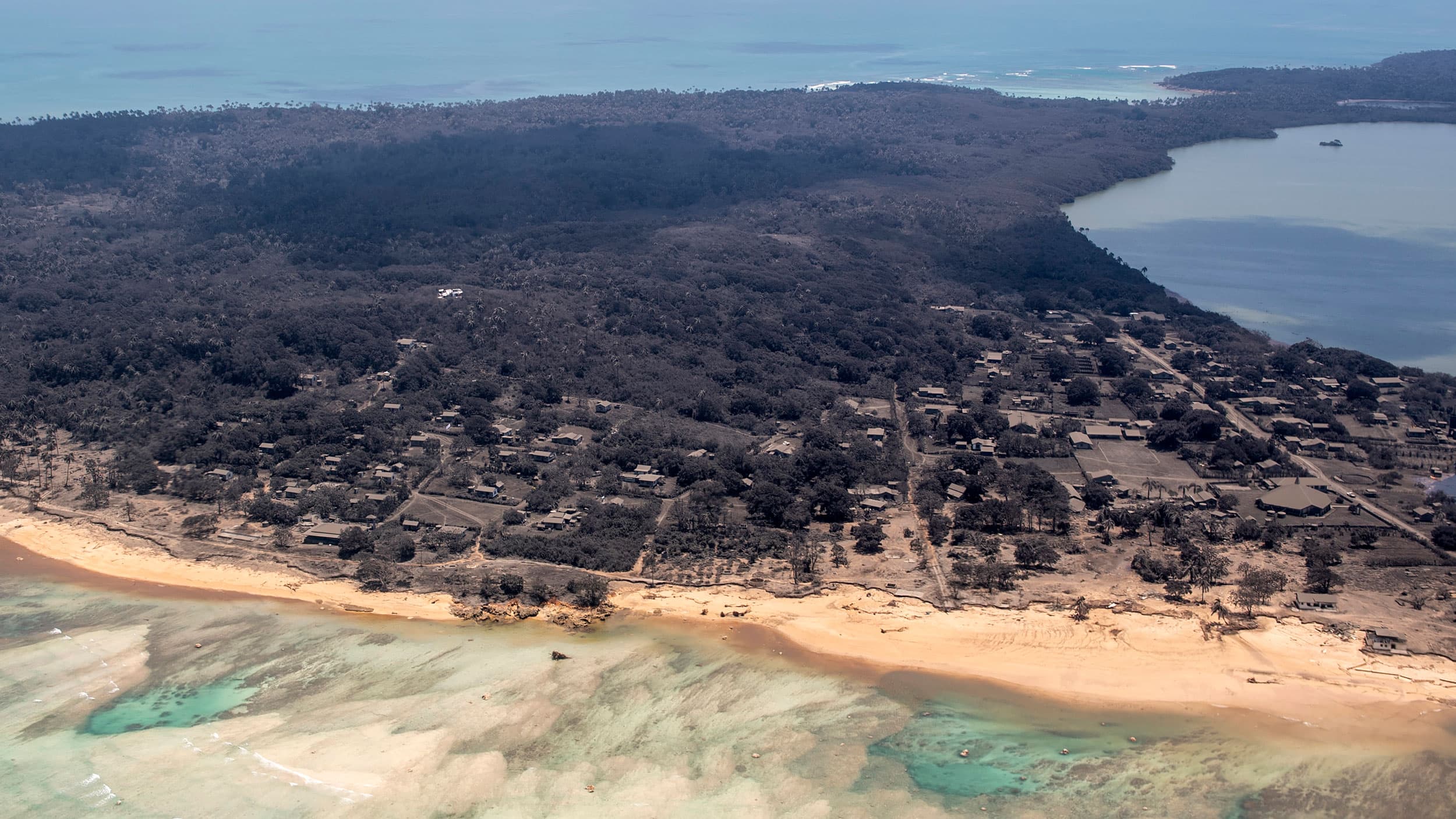 In this photo provided by the New Zealand Defense Force, volcanic ash covers roof tops and vegetation in an area of Tonga, Monday, Jan. 17, 2022.