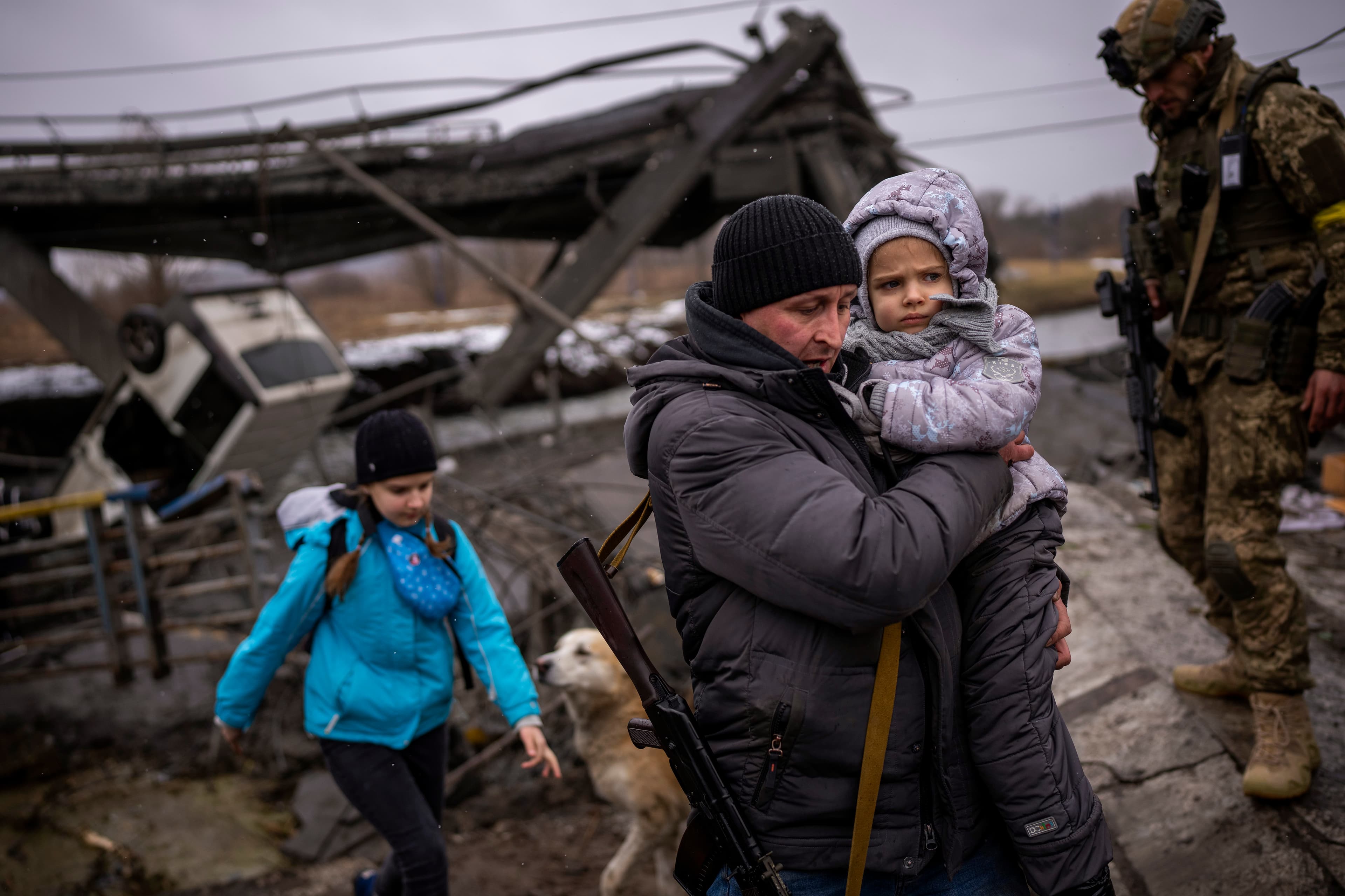 Local militiaman Valery, 37, carries a child as he helps a fleeing family across a bridge destroyed by artillery, on the outskirts of Kyiv, Ukraine, on Wed., March 2, 2022.