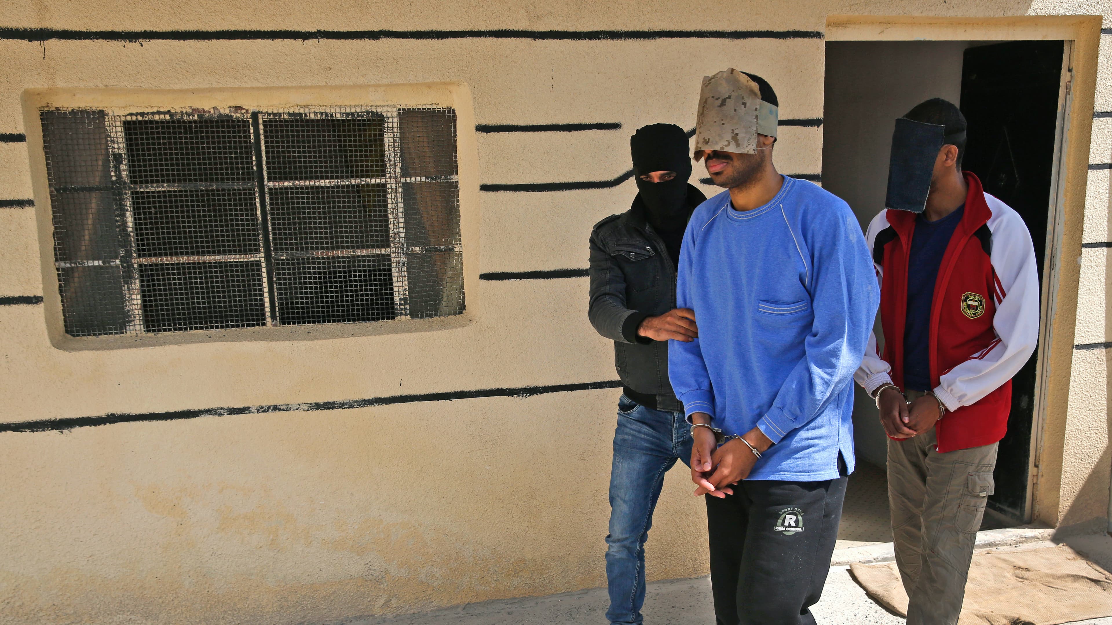 A Kurdish security officer escorts Alexanda Kotey, left, and El Shafee Elsheikh