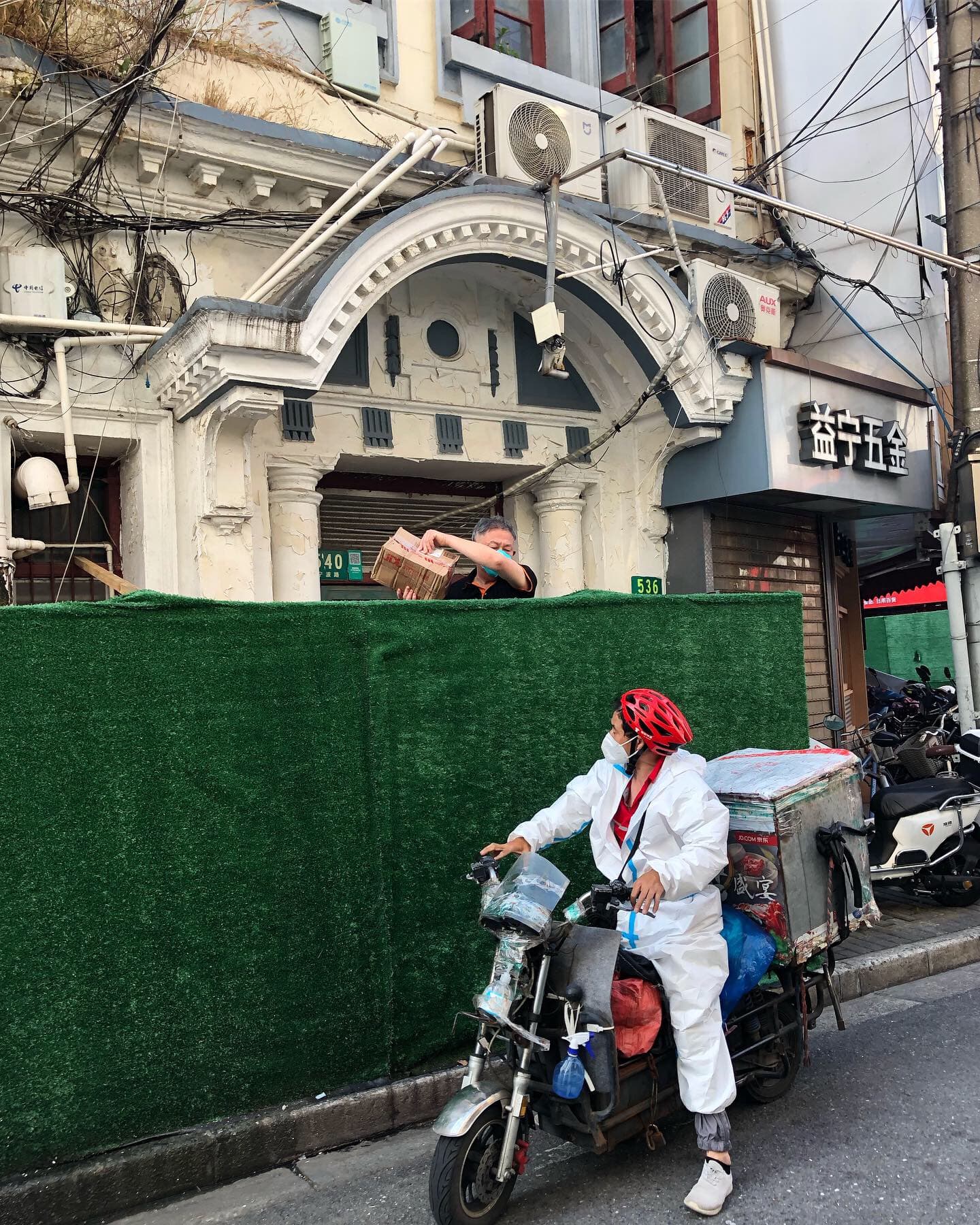 A man receives a package from behind the fence that blocks his apartment in a Shanghai neighborhood