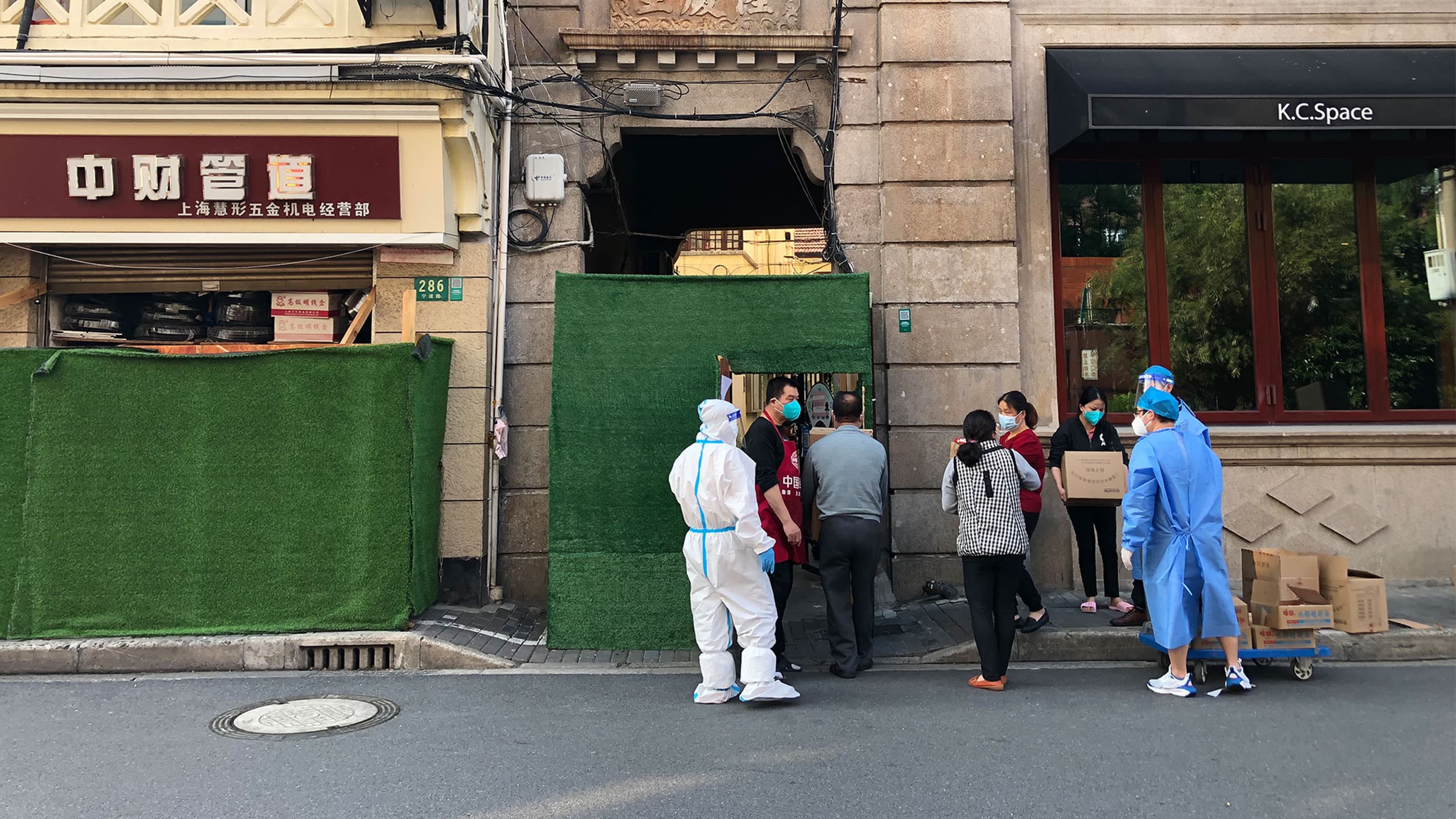 Residents in a sealed-off Shanghai neighborhood receive bulk-ordered food supplies under the monitoring of health workers in hazmat suits