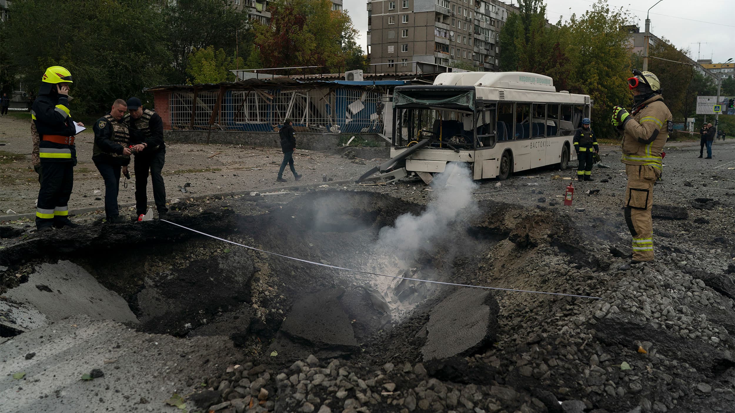 Firefighters and police officers work on a site where an explosion created a crater on the street after a Russian attack in Dnipro, Ukraine