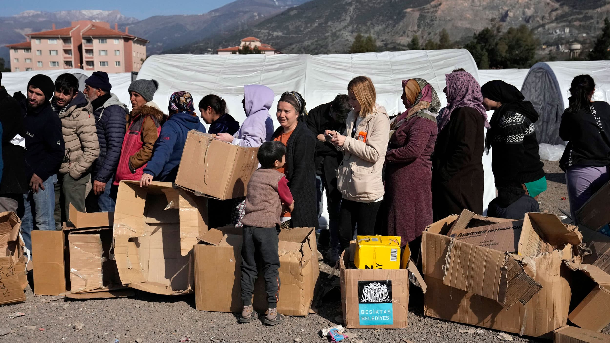 People who lost their houses in the devastating earthquake, lineup to receive aid supplies at a makeshift camp, in Iskenderun city, southern Turkey, Tuesday, Feb. 14, 2023.
