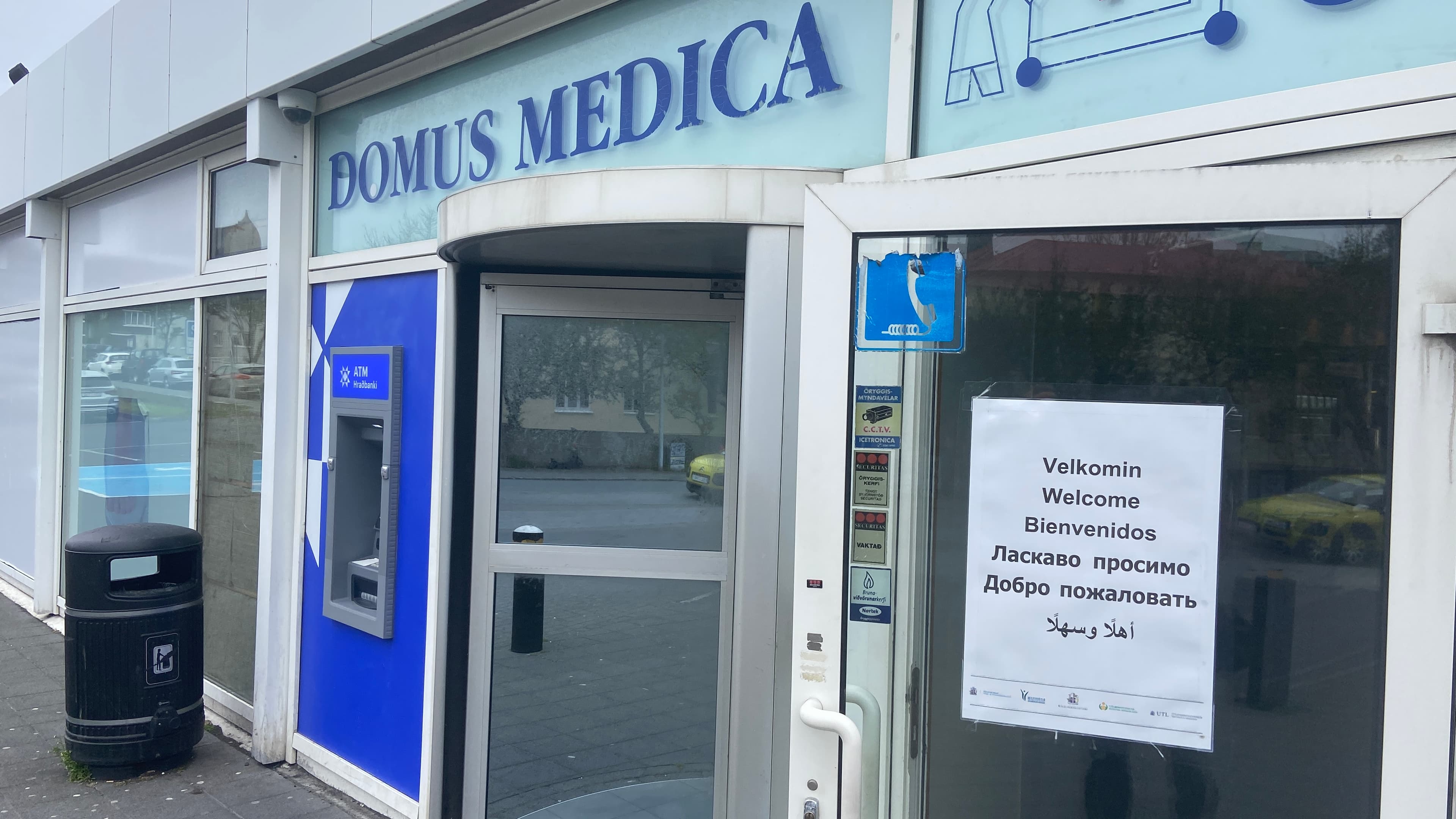 a sign outside of a clinic welcomes asylum seekers in various languages