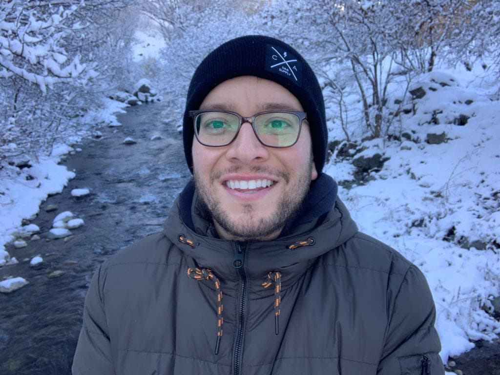 close-up of a man smiling, wearing winter gear in a snowy forest