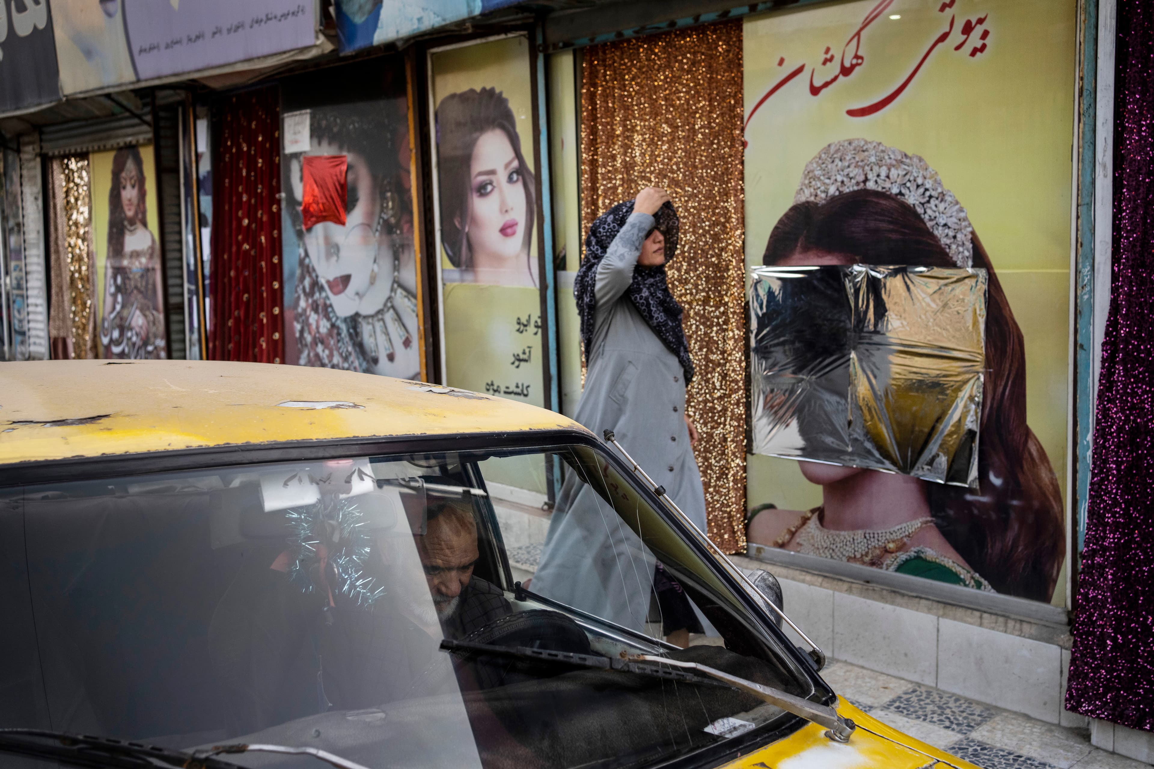 A tax cab in the forefront of a woman walking down the street past a closed beauty salon