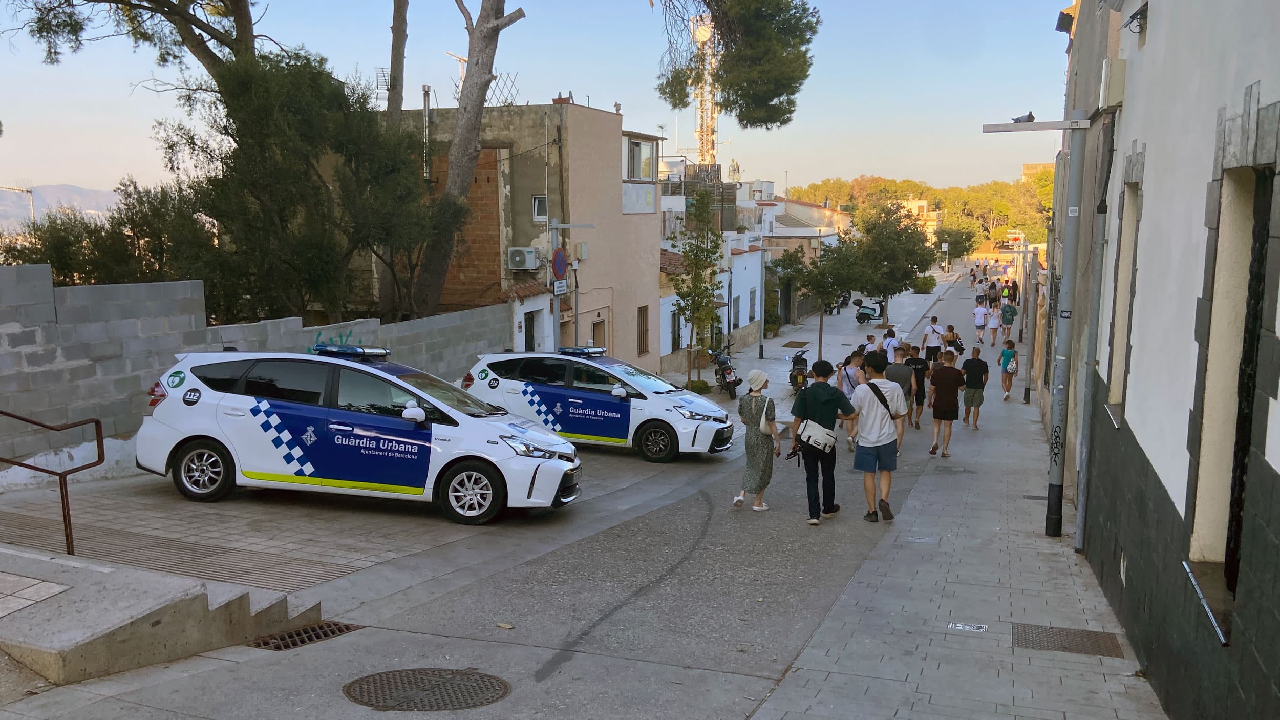 Police cars park along a street with people passing by.