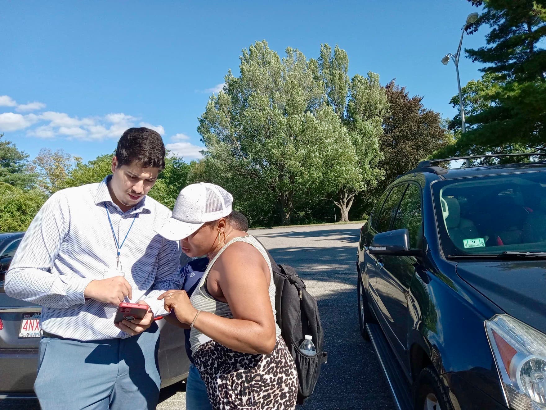 Man and woman with a baseball cap stand and talk in parking lot