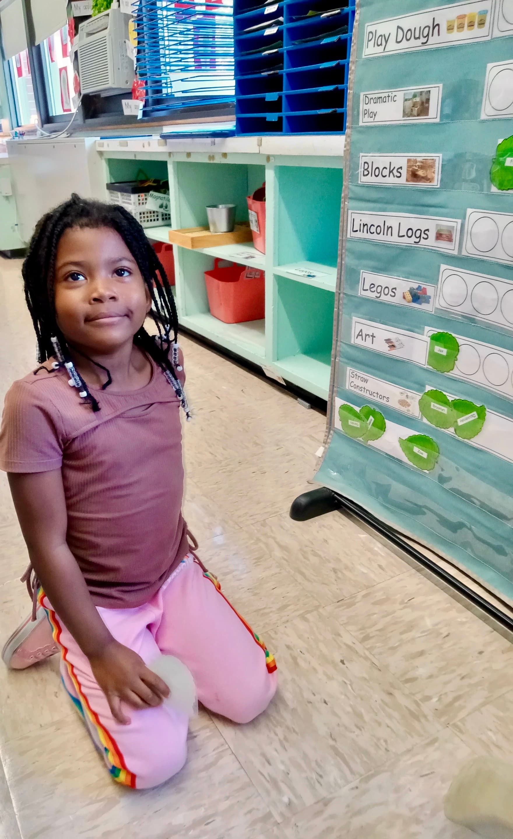 A young girl in a classroom wearing magenta clothing and posing for a photo