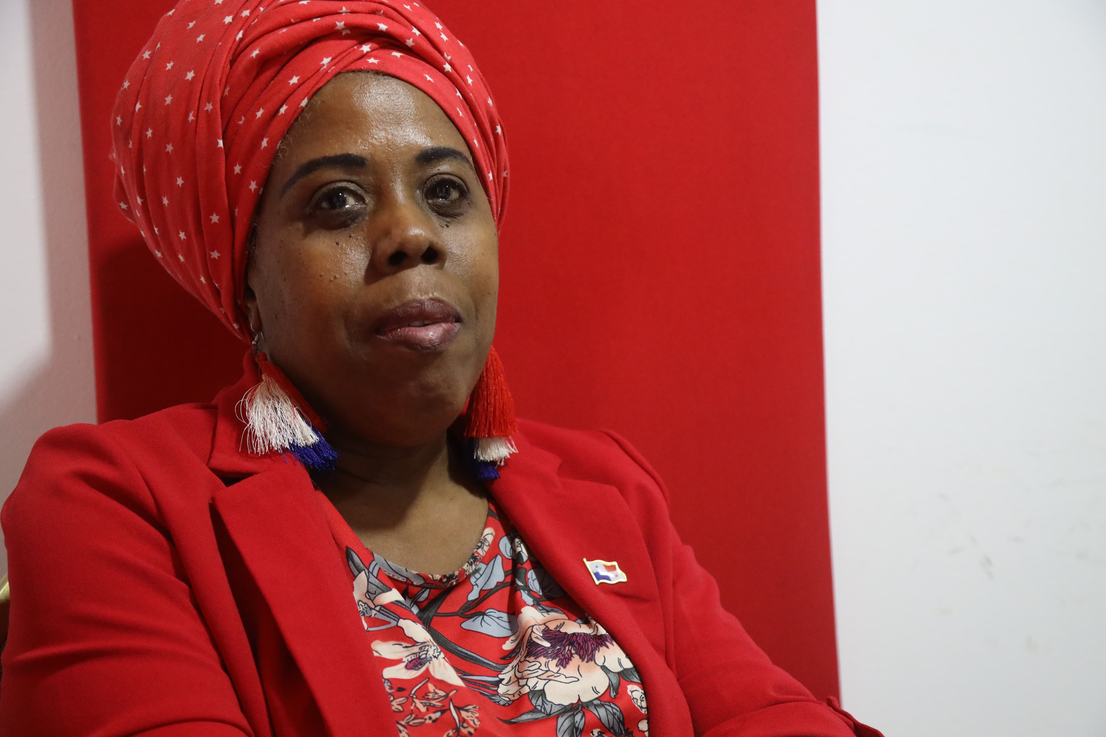 An older Black woman with a red blazer and head wrap