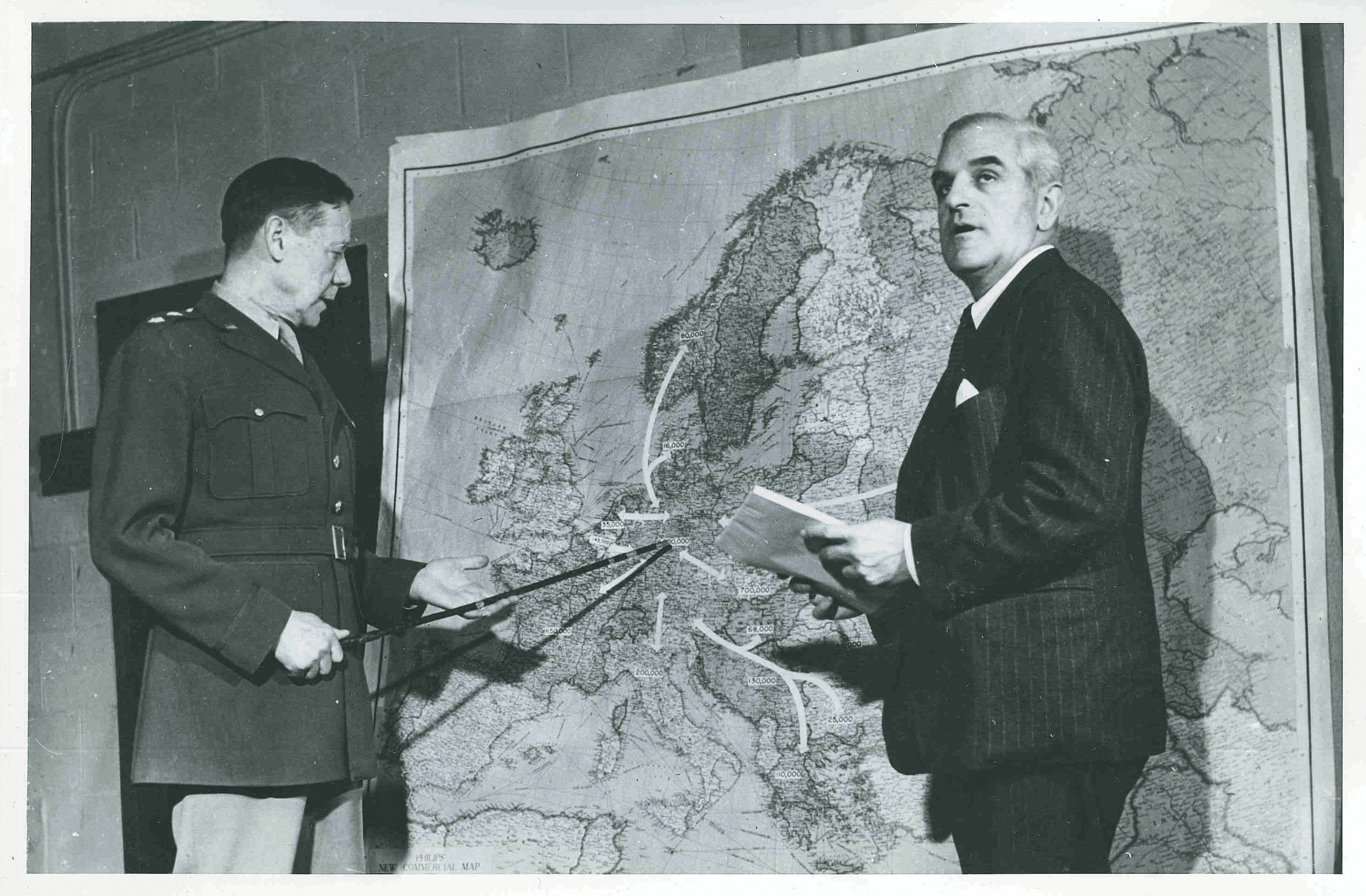 Two men point and look at a map, in black and white