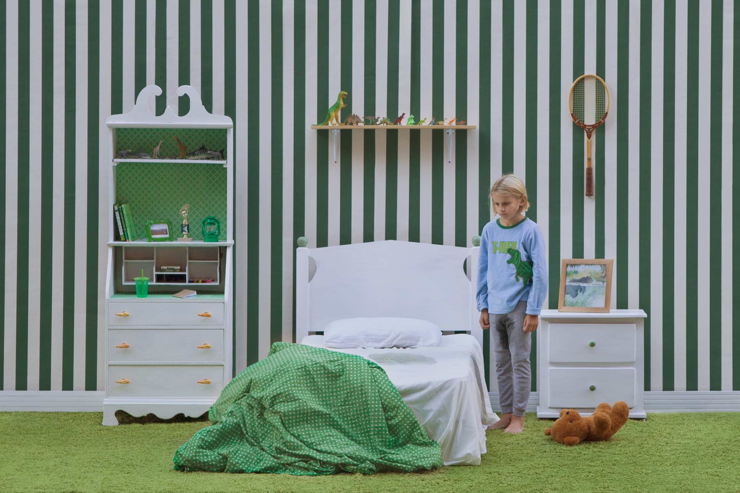 A boy in soaking pajamas looks down at the bed he just wet.