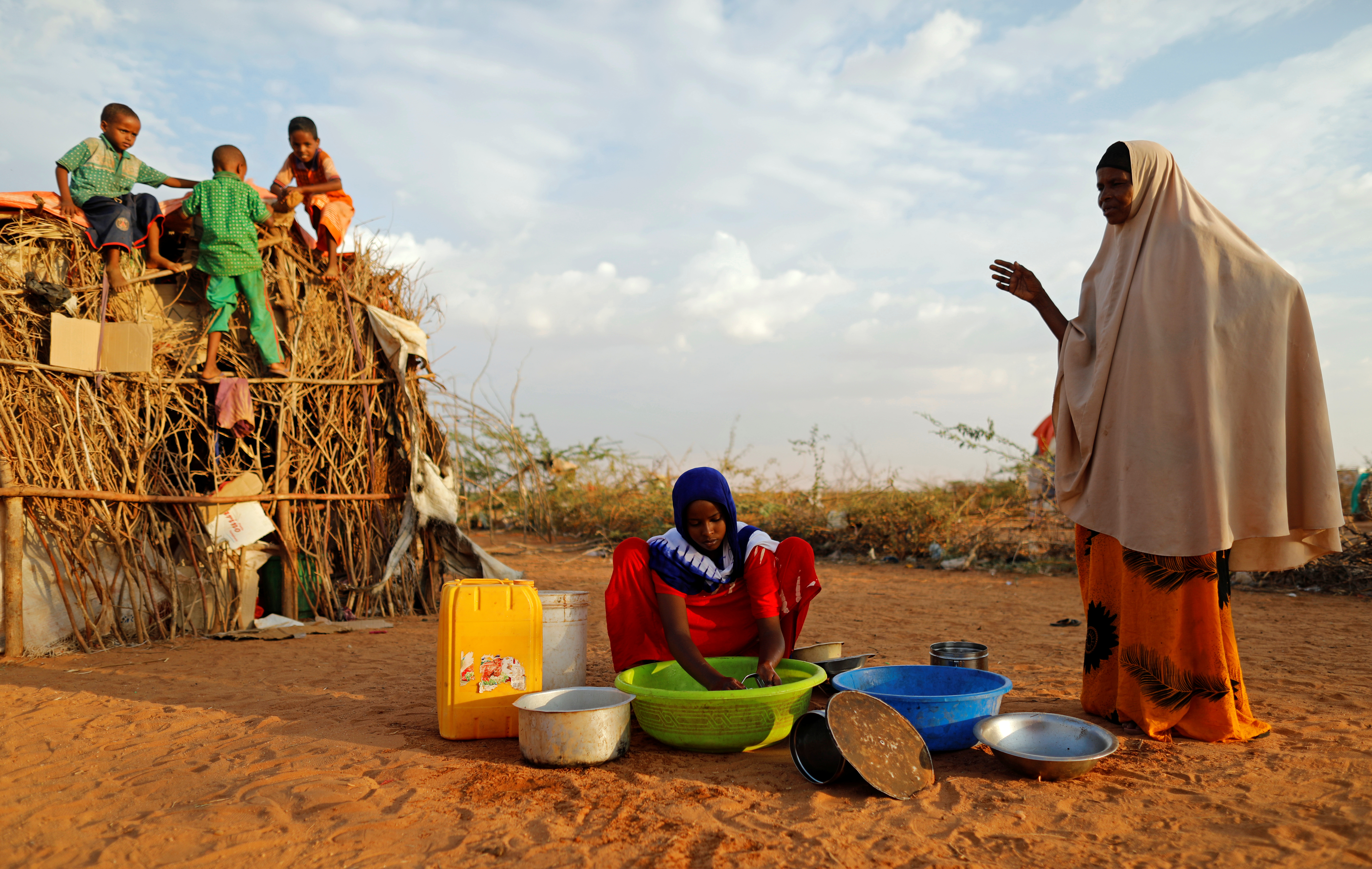 Zeinab, 14, washes dishes alongside her mother Abdir Hussein while her nephews play at a camp for internally displaced people in Dolow, Somalia April 3, 2017.