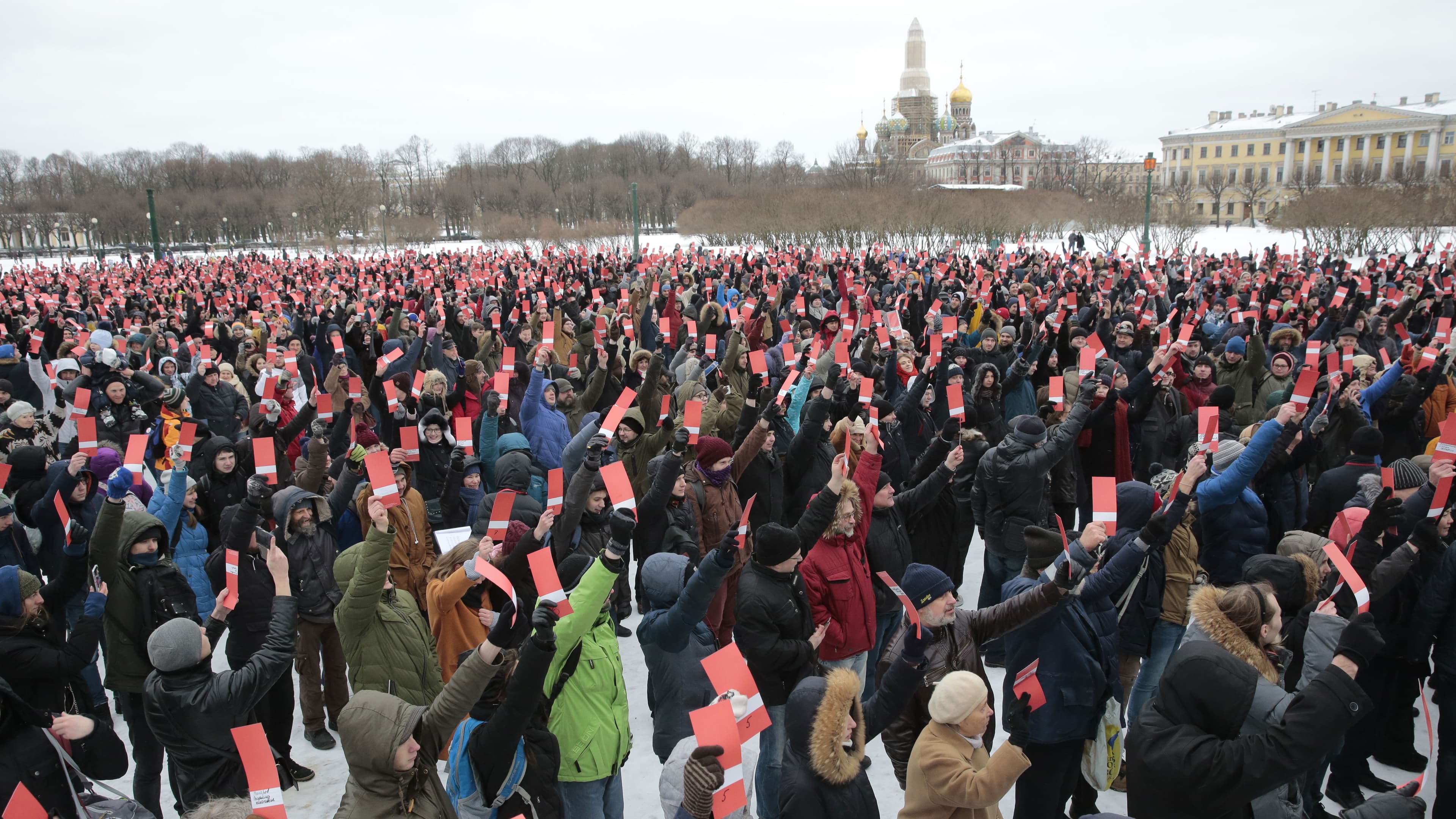 A crowd of people hold up red cards showing their support for Alexia Navalny. Behind them are some of St. Petersburg's famous landmarks.