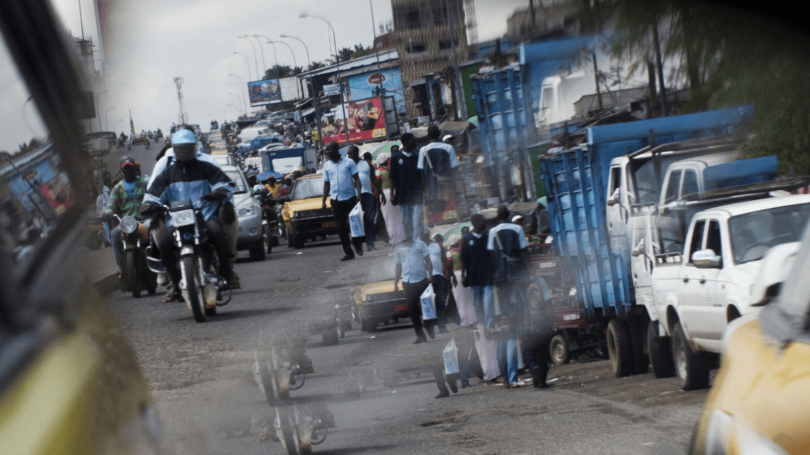A reflection from the wing mirror of a car shows people ride motorcycles in Douala.