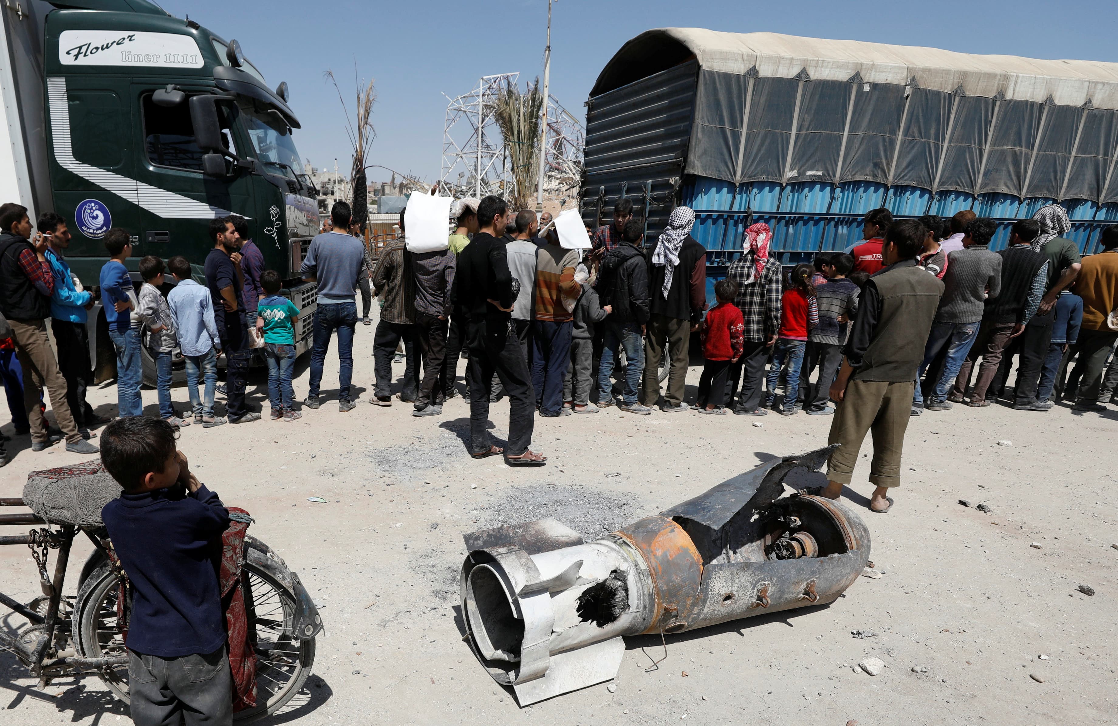 A boy stands next to the remains of a missile as people line up for aid in the city of Douma in Damascus, Syria, on April 16, 2018.