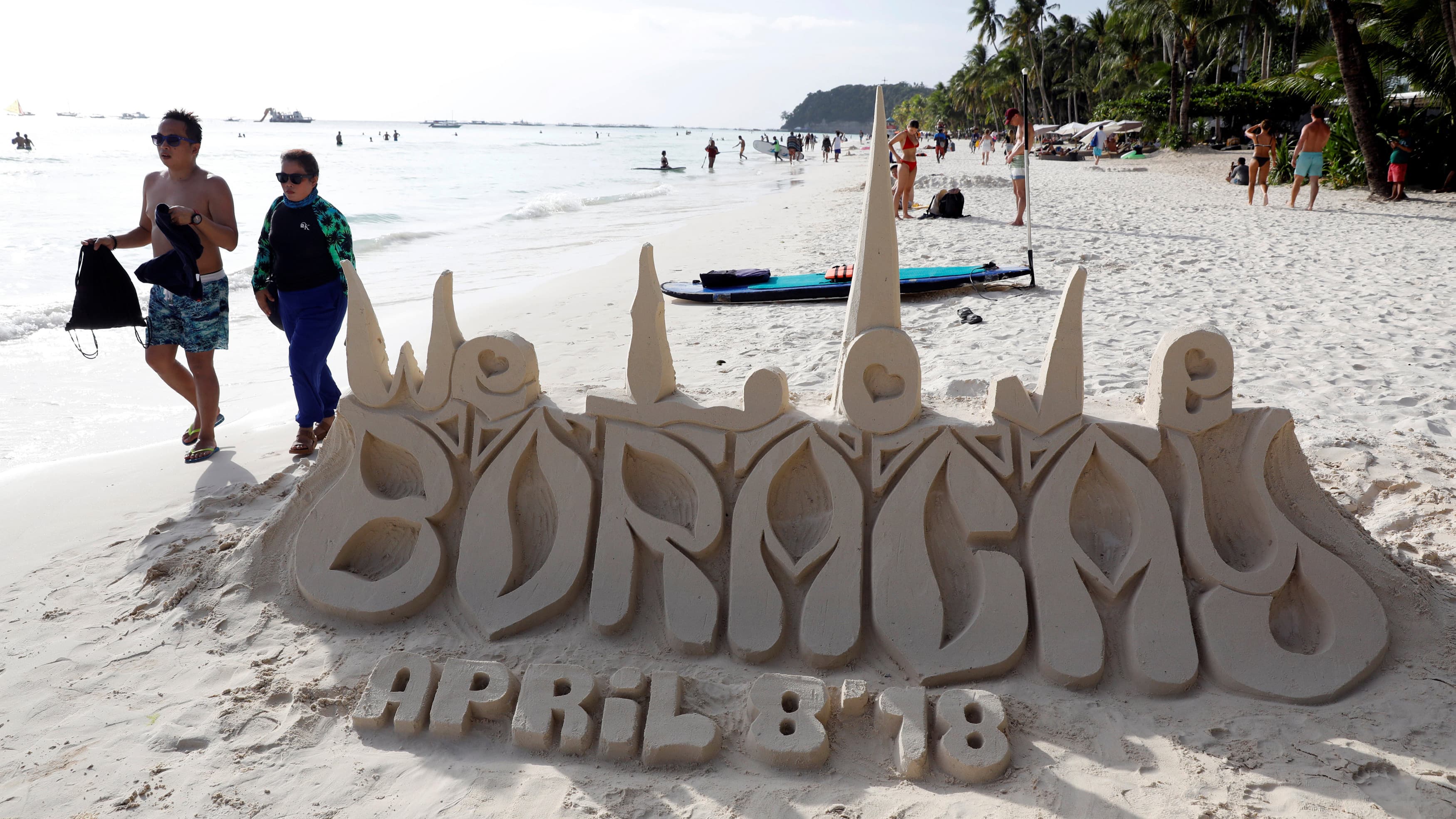 A sand sculpture reads Boracay April 8, 2018, as tourists wander by.