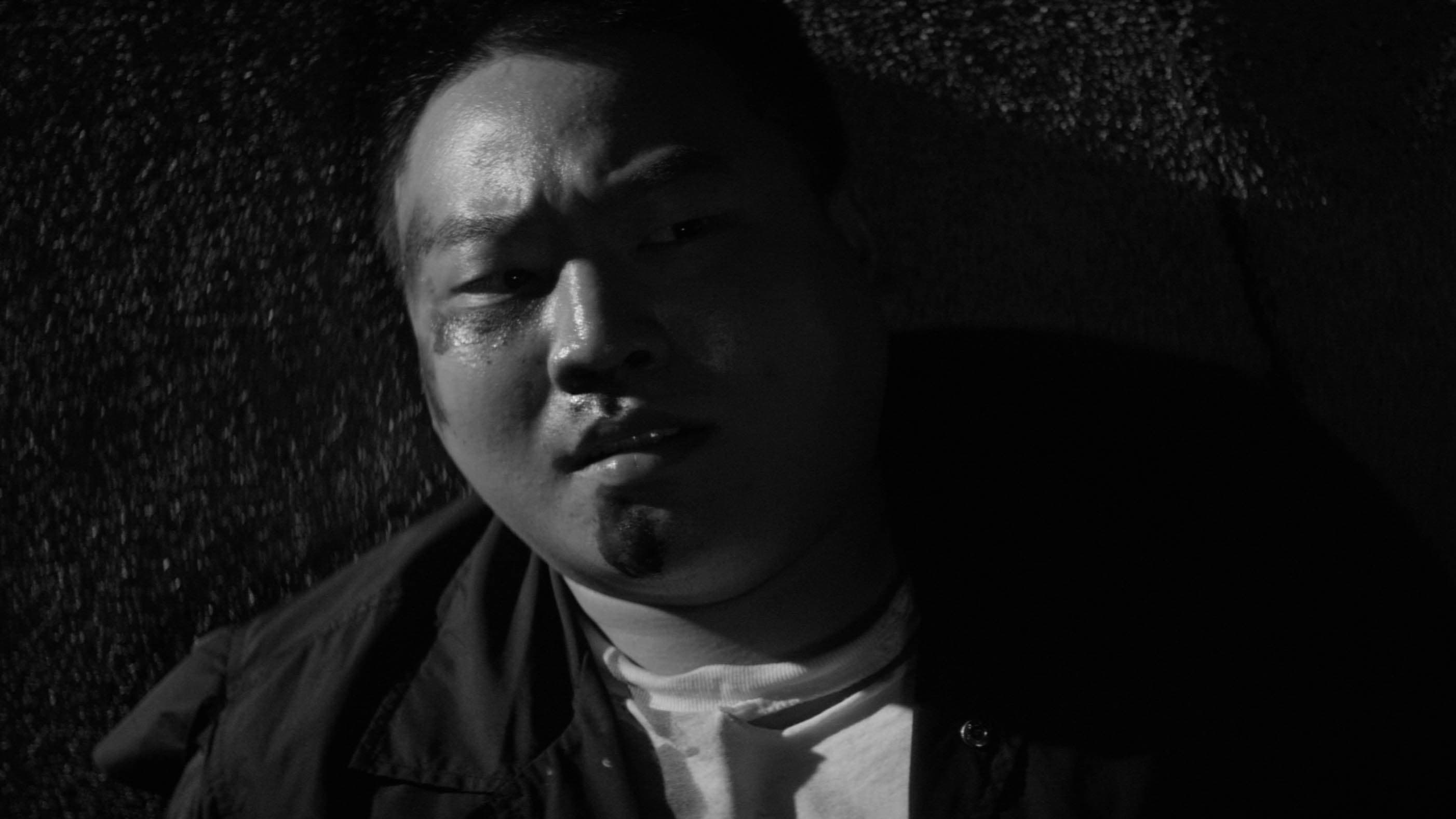 Man with beaten face on pavement, black and white still