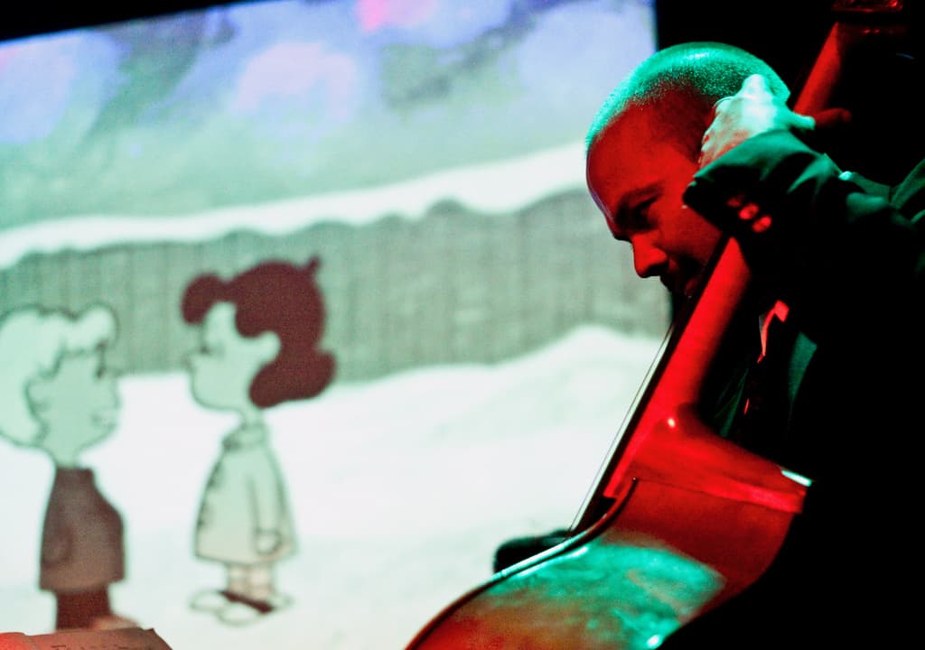 "A Charlie Brown Christmas" plays on screen behind a live band.