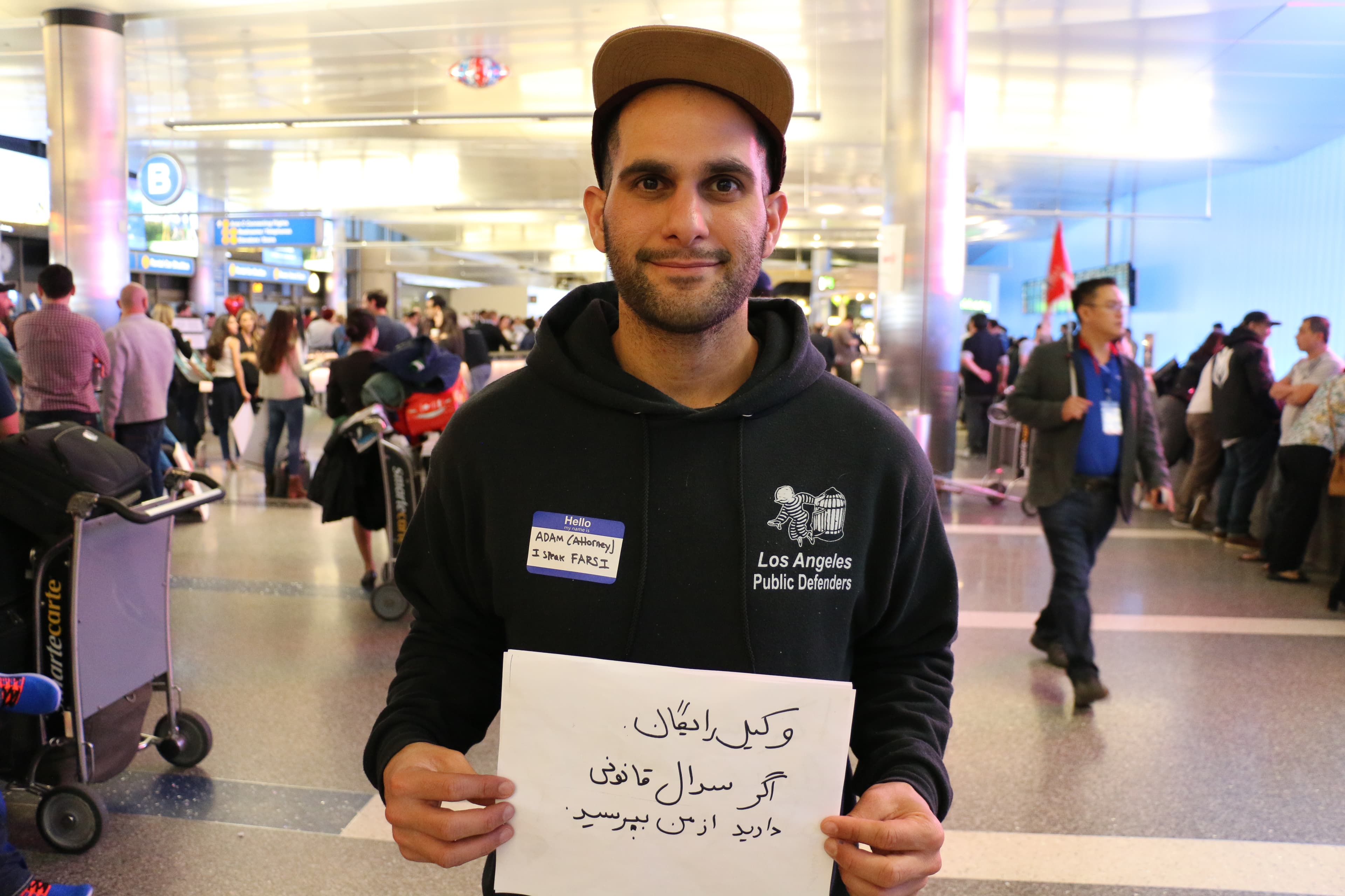 Man in sweatshirt with public defenders logo holds sign in Arabic