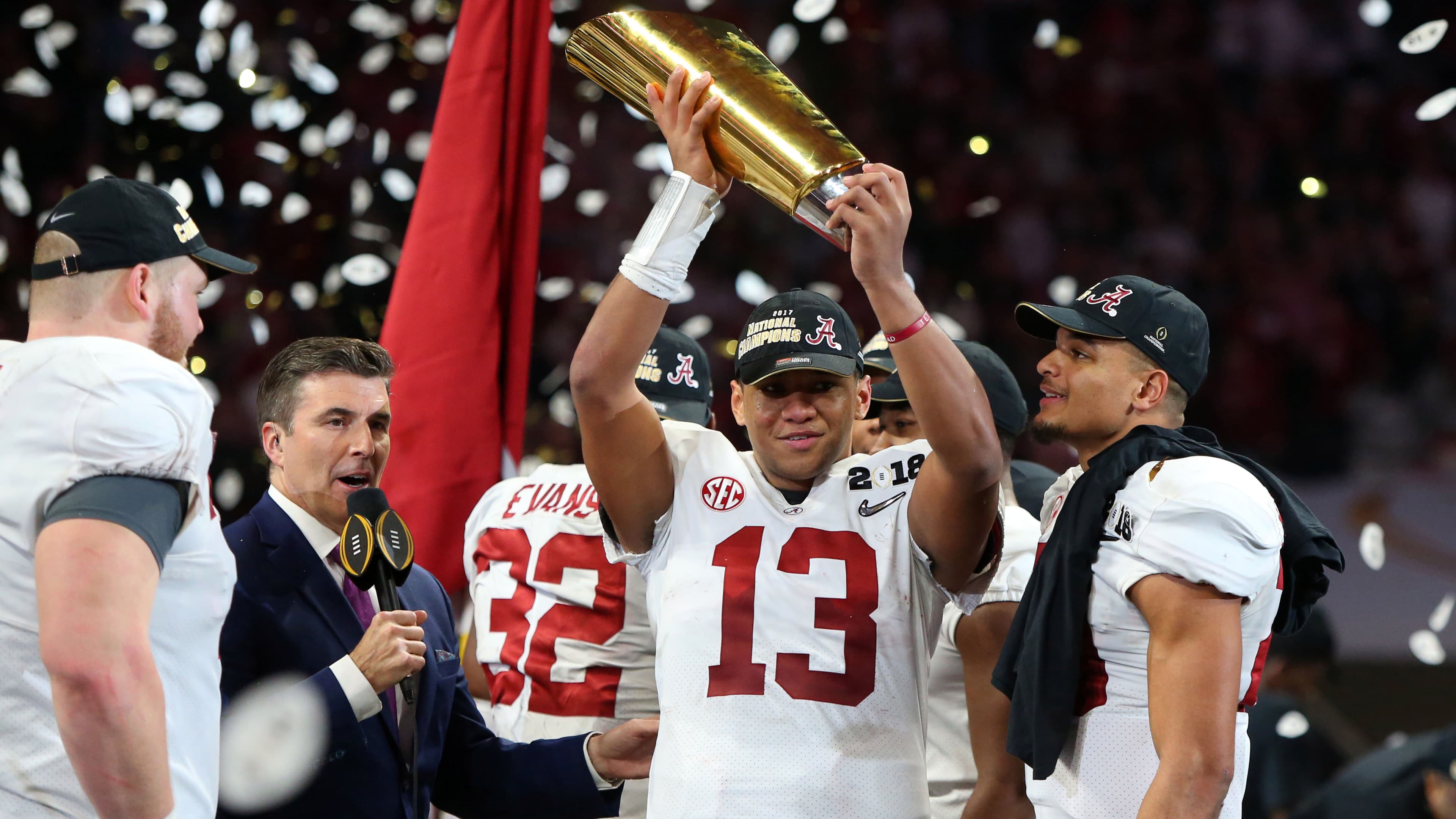A man in a football jersey holds a trophy over his head as confetti rains down behind him.
