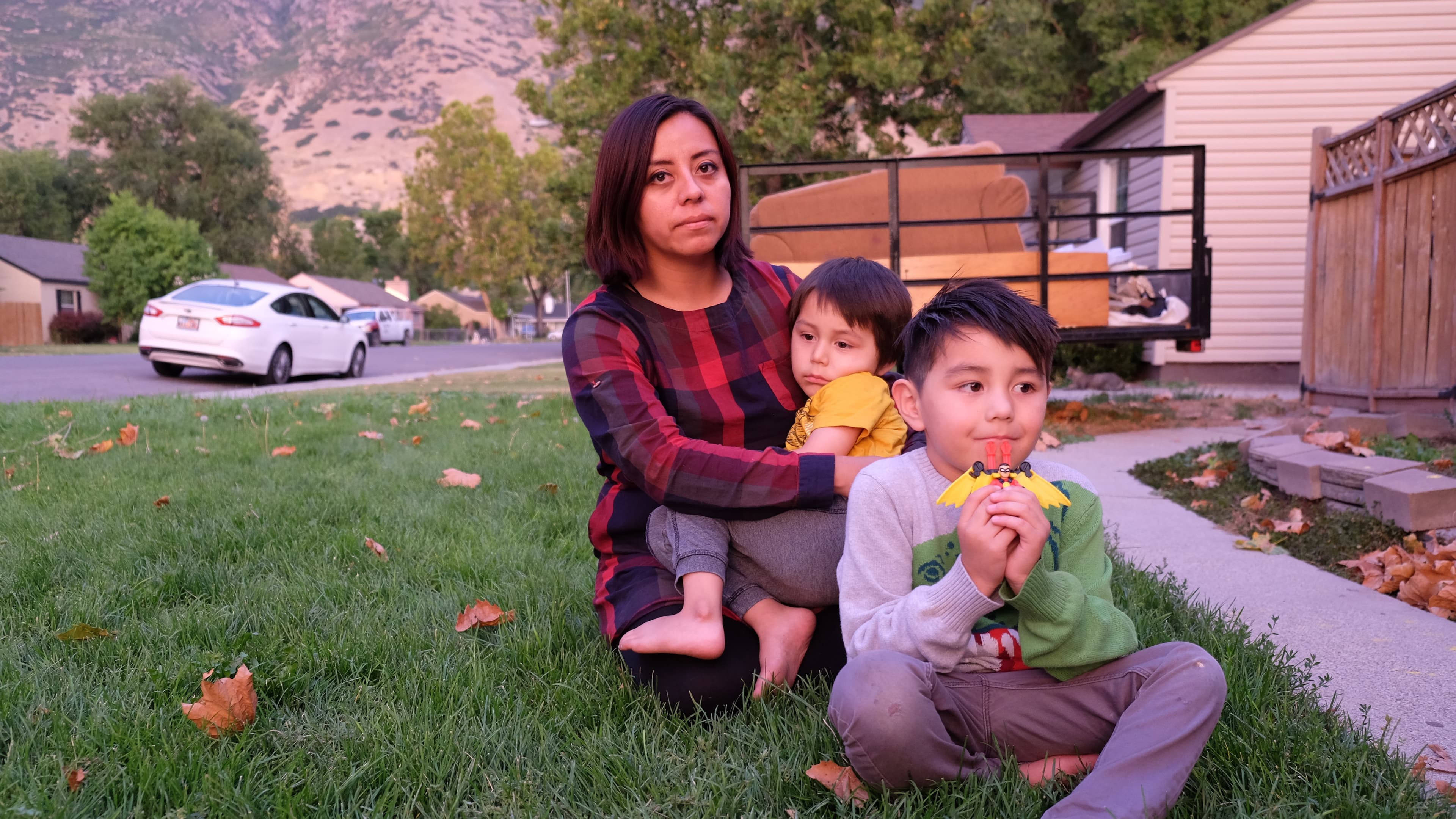 Woman sitting on grass in front of building with two young children in front of her