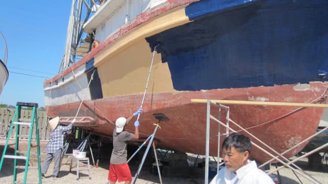 Sang Ho and crew paint his shrimping boat for shrimping season. He now also farms in addition to shrimp fishing.
