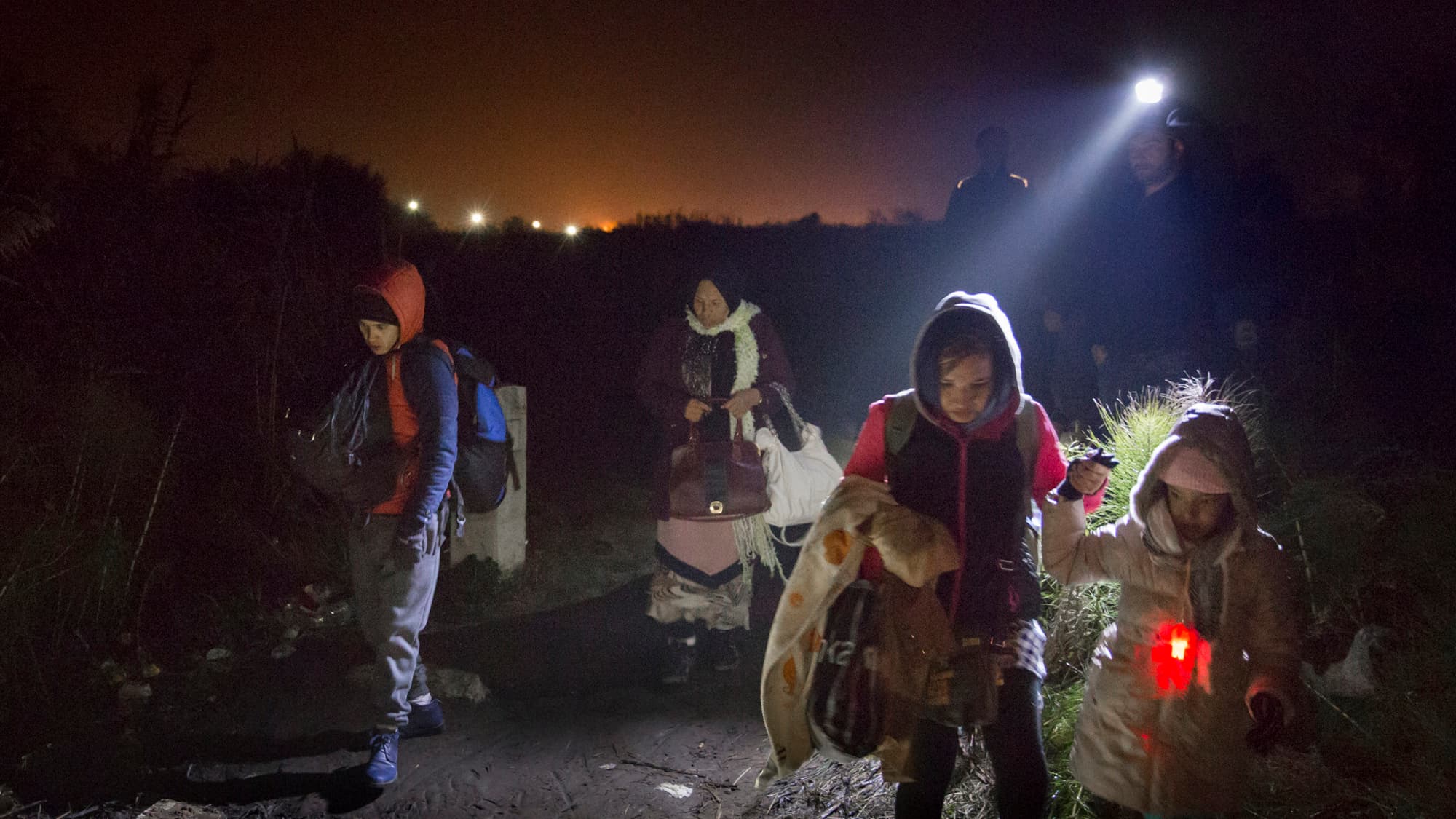 Thousands of migrants and refugees arrive daily by train into Tabonovzce, Macedonia, on their way north. Volunteers with flashlights illuminate their path as they walk to an informal crossing point into Serbia.