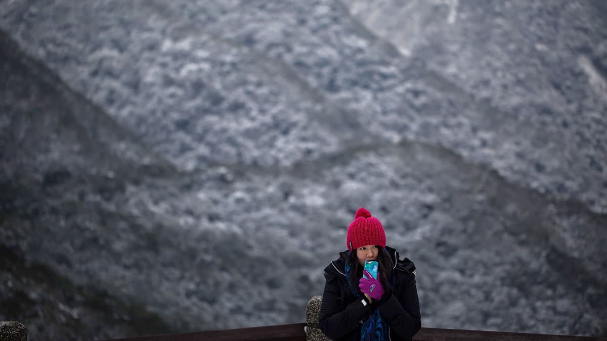 A woman takes photographs as snow is seen at the background on the Yangmungshan National Park during a snowfall in Taipei, Taiwan. Taiwan experienced a sudden drop in temperature over the weekend.
