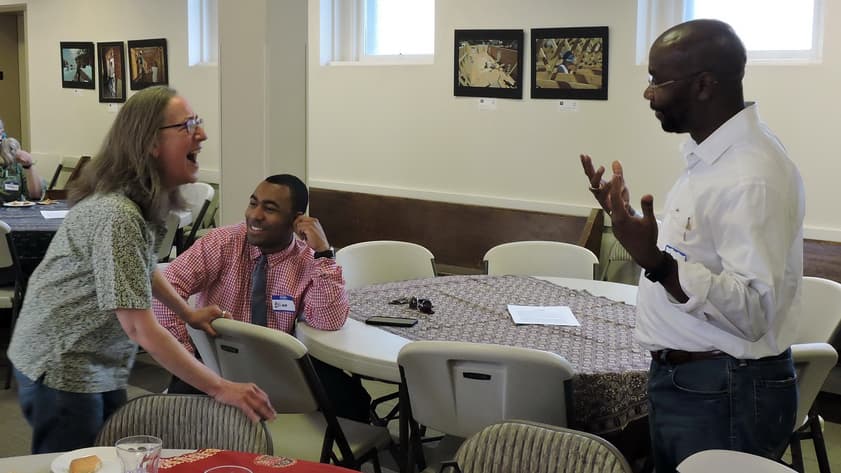 Wilmot Collins gestures across table to a woman who he is speaking with