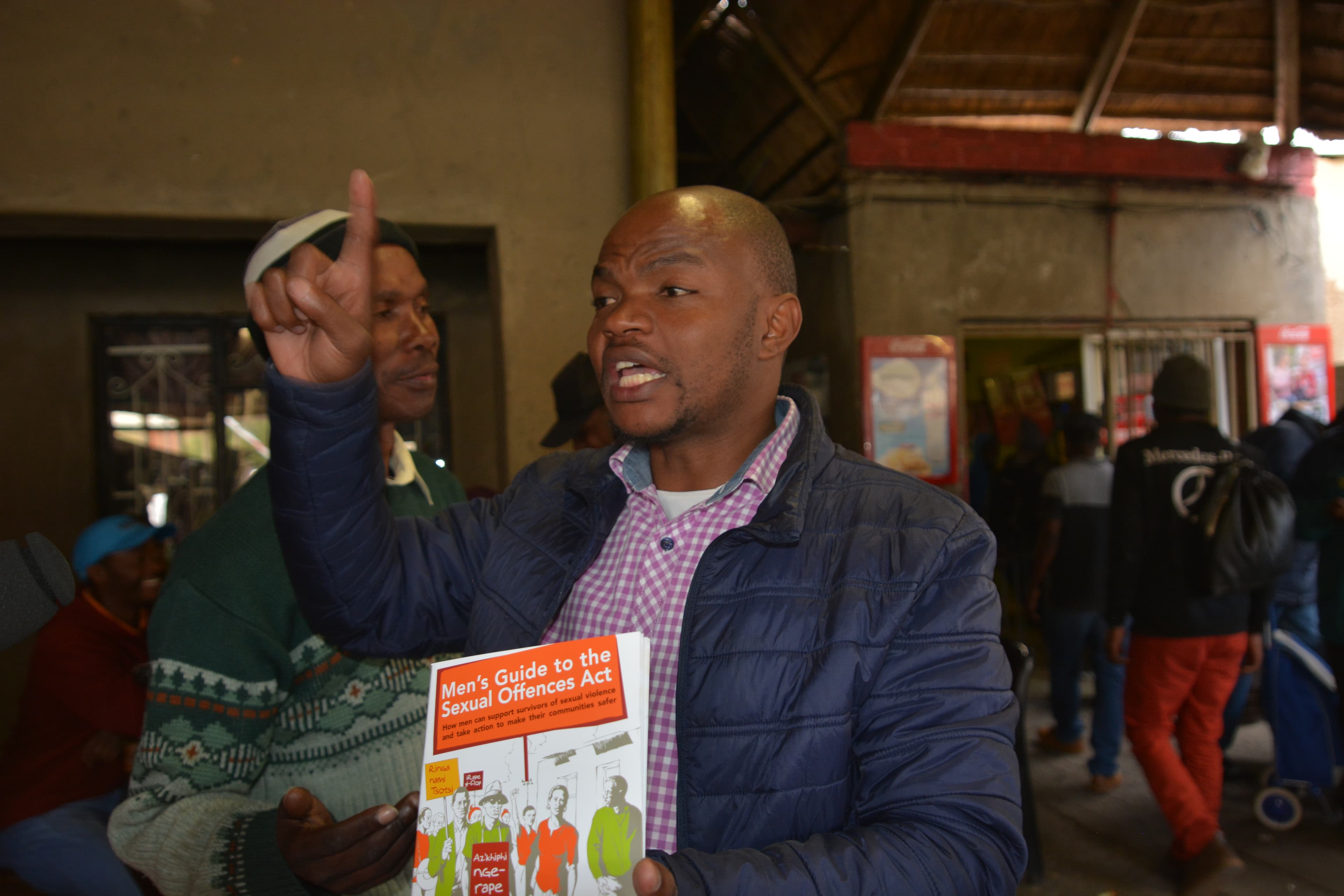 Abu-Baker Sebeela stands in a tavern holding up a pamphlet
