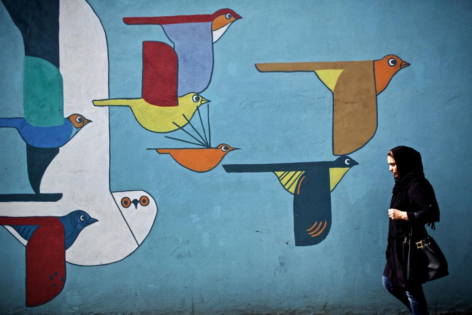 An Iranian woman walks past a mural in Tehran on June 29, 2015.