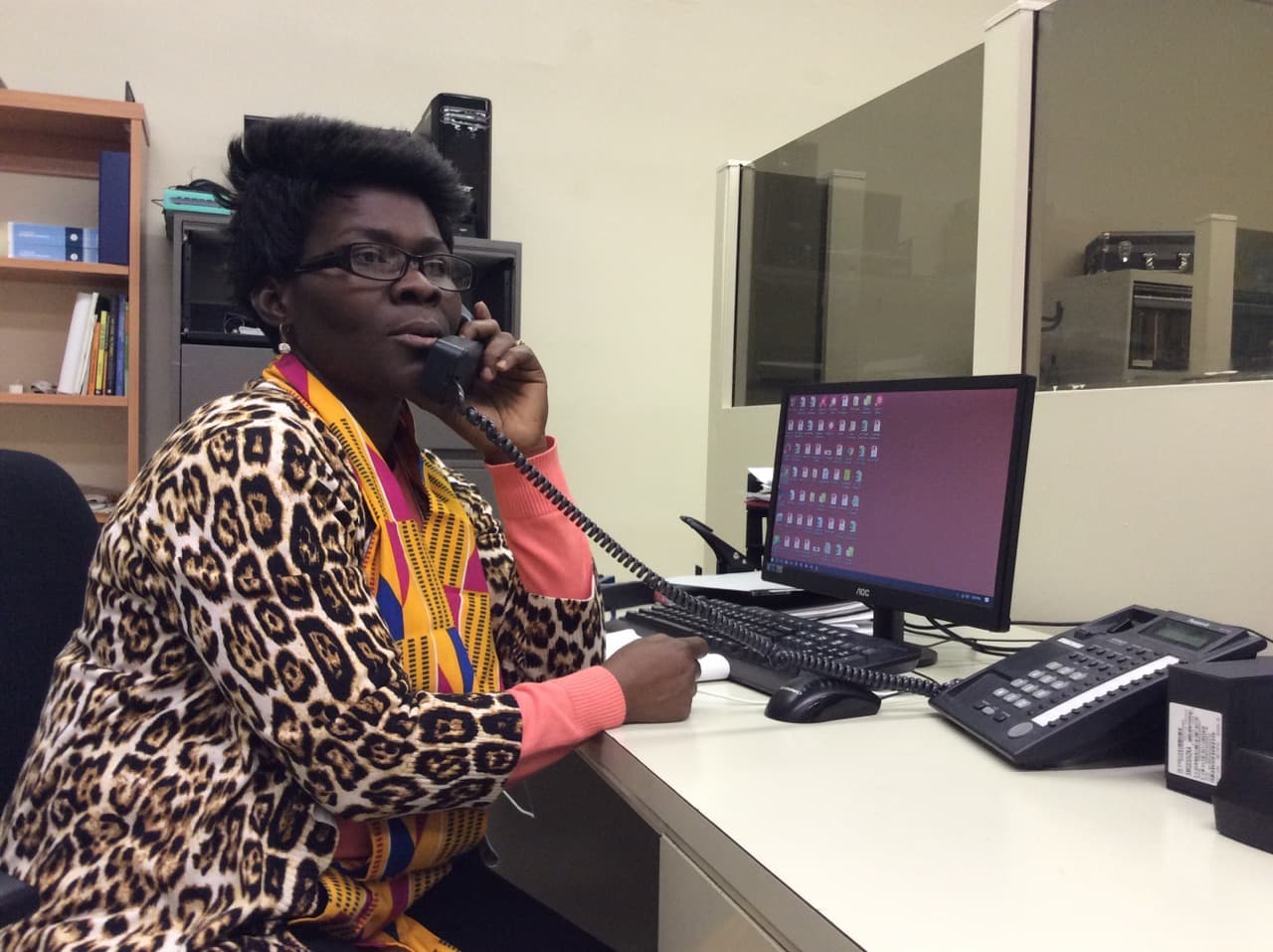 Woman sitting at desk while on phone, with computer screen behind