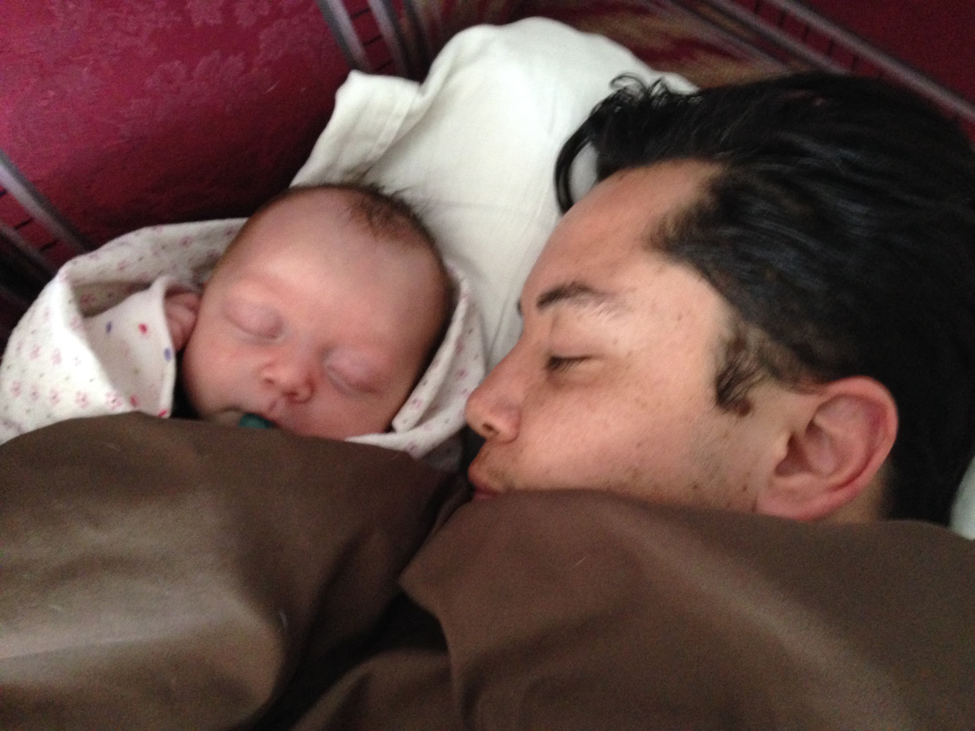 Close-up of face of man asleep on sofa with infant child next to him, wrapped in blanket