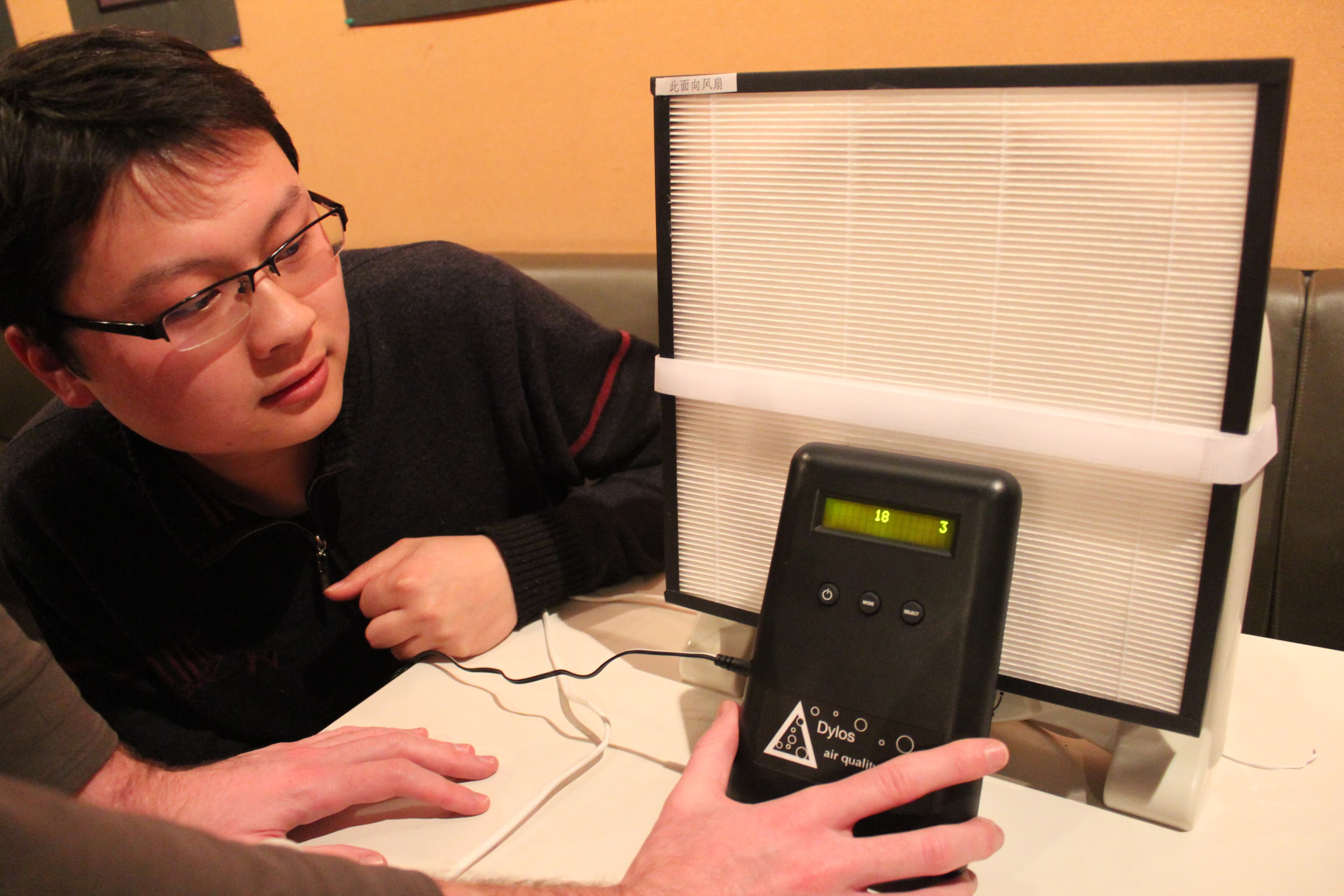 A group of people gather at a coffee shop in Shanghai to learn how to put together simple air filters with a fan and velcro.