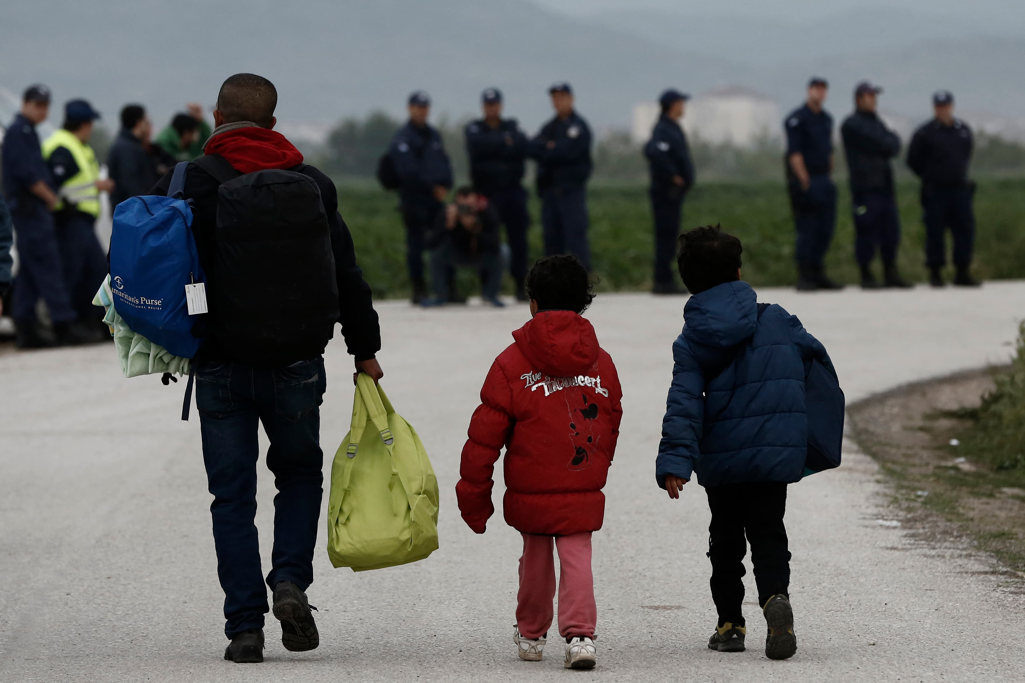 Refugees carry their belongings in front of riot policemen during a police operation at a refugee camp at the border between Greece and Macedonia, near the village of Idomeni, Greece, 24 May 2016.