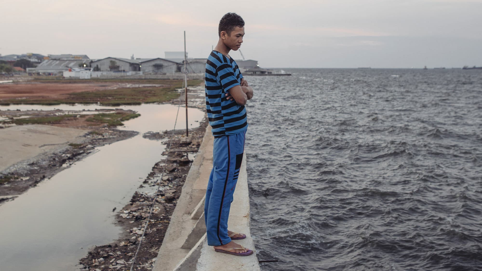 Feri Yadi, a resident of Muara Baru in North Jakarta, stands atop the seawall recently built to protect his neighborhood. He has little confidence that the wall will work as expected. "Like in the past, this will be broken somehow" he says.