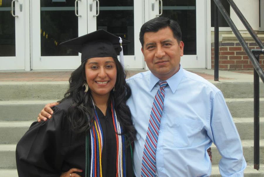 Portrait of woman in graduation cap and gown with man whose are is around her shoulder
