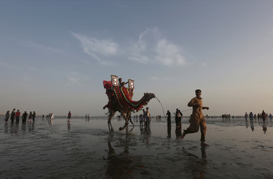 A man leads a camel with children taking a ride on it along the Clifton beach in Karachi, Pakistan