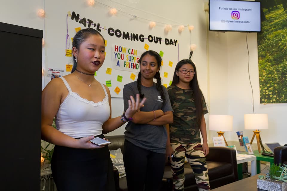 A student speaking in front of a board of post-it notes, with two other students standing nearby