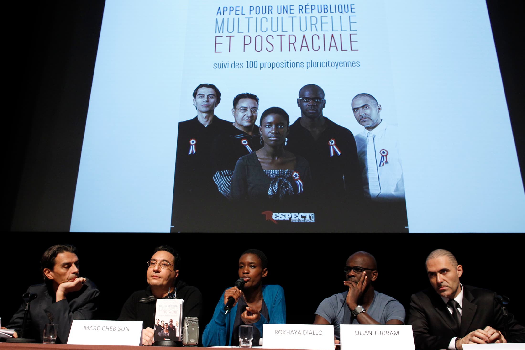 Rokhaya Diallo speaking on a panel below a screen that says in French, 'call for a multicultural and postracial republic'