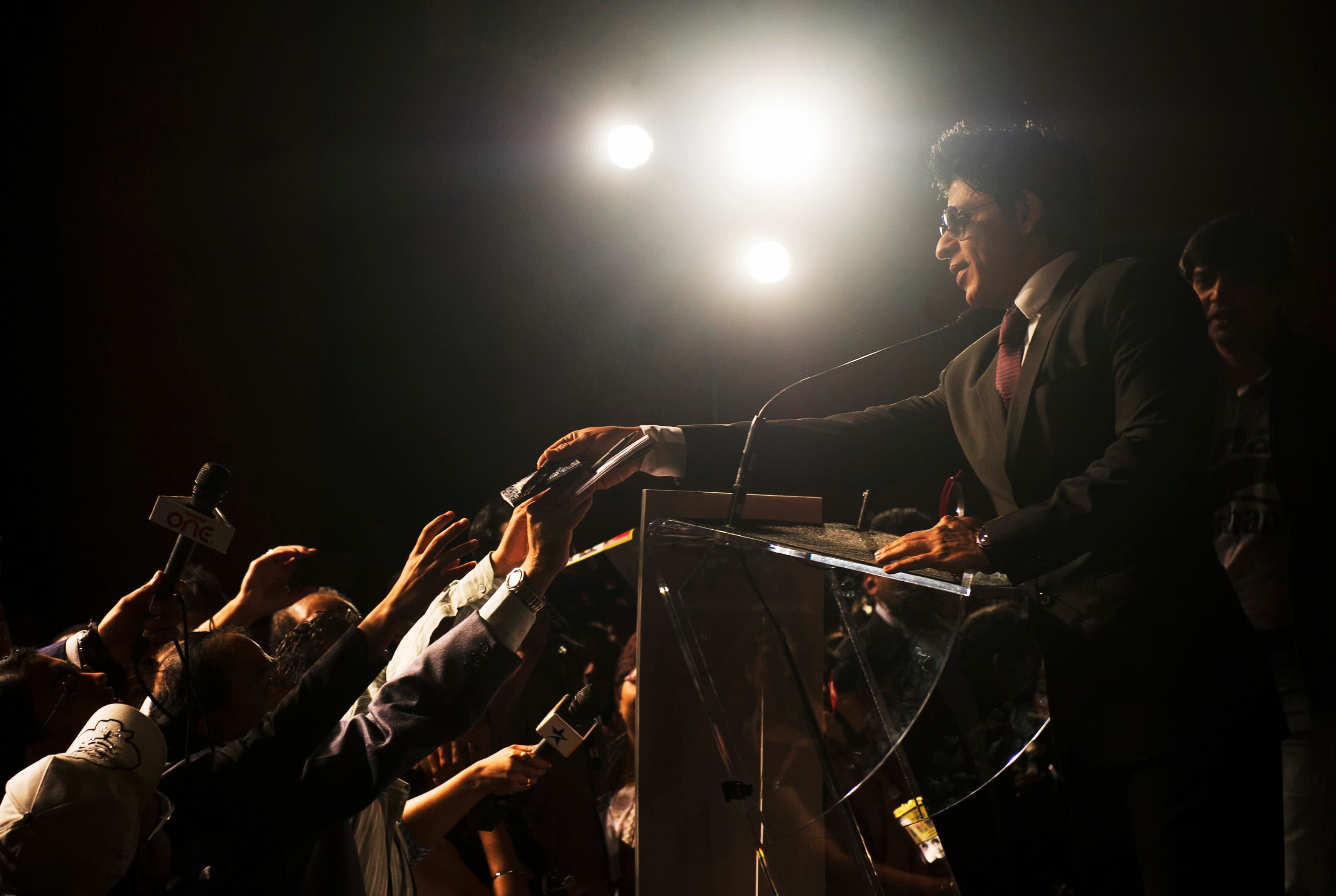 Man in sunglasses reaches out to crowd, with flashes from photographers
