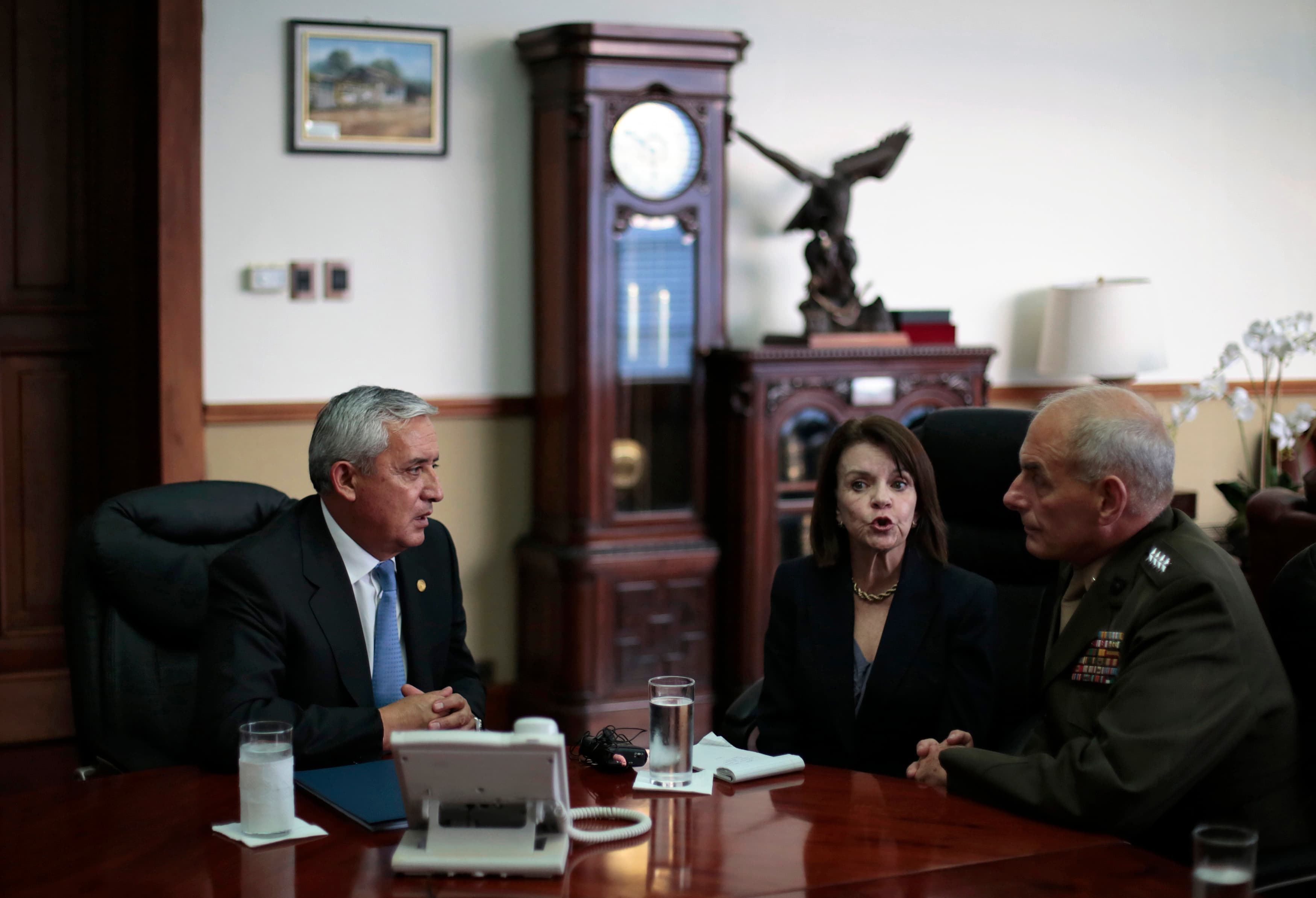 Two men speaking at a desk, with a woman sitting between translating