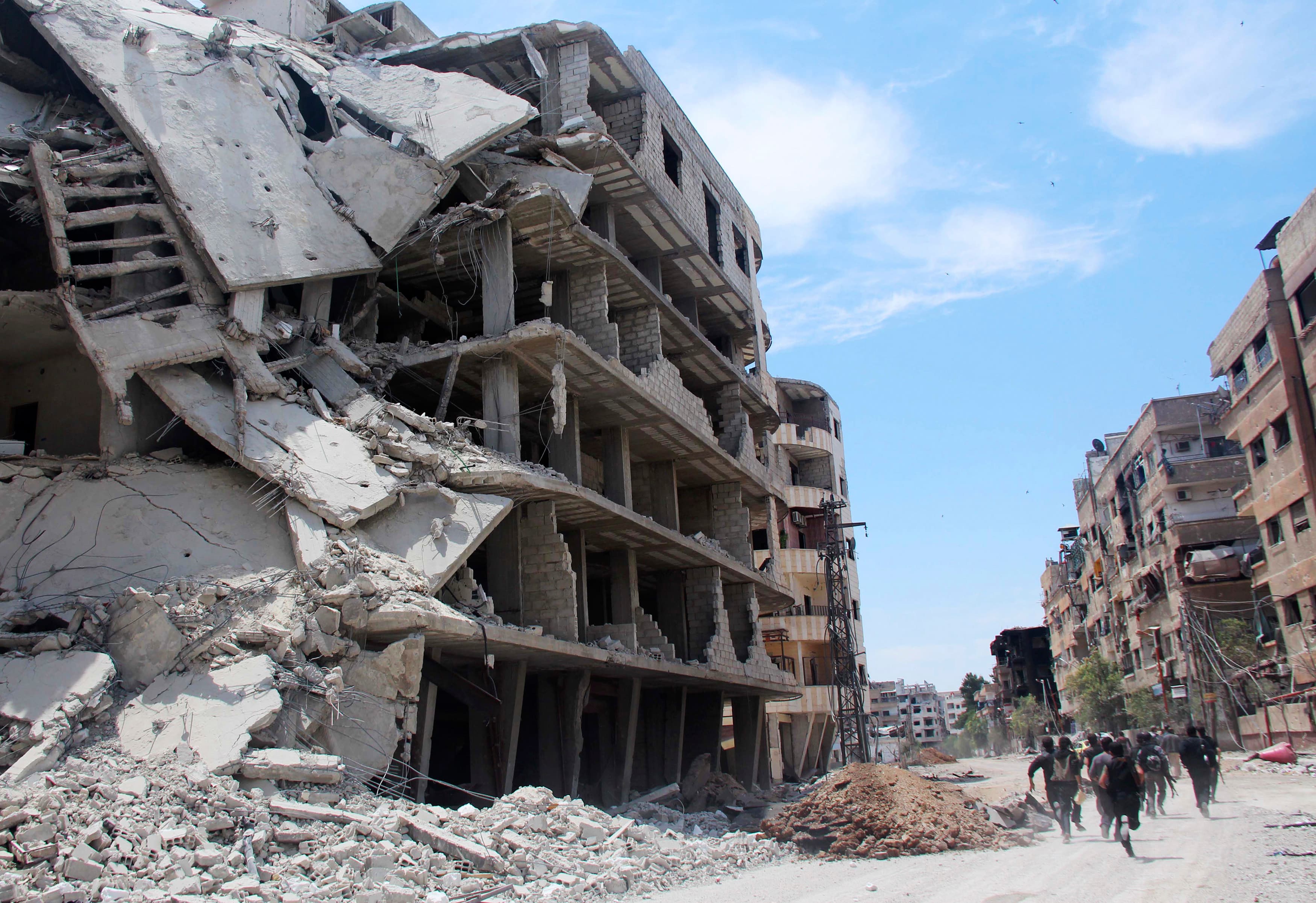 Rebel fighters carry their weapons as they run past damaged buildings to avoid snipers loyal to Syria's President Bashar al-Assad in the Mleha suburb of Damascus on May 26, 2014.