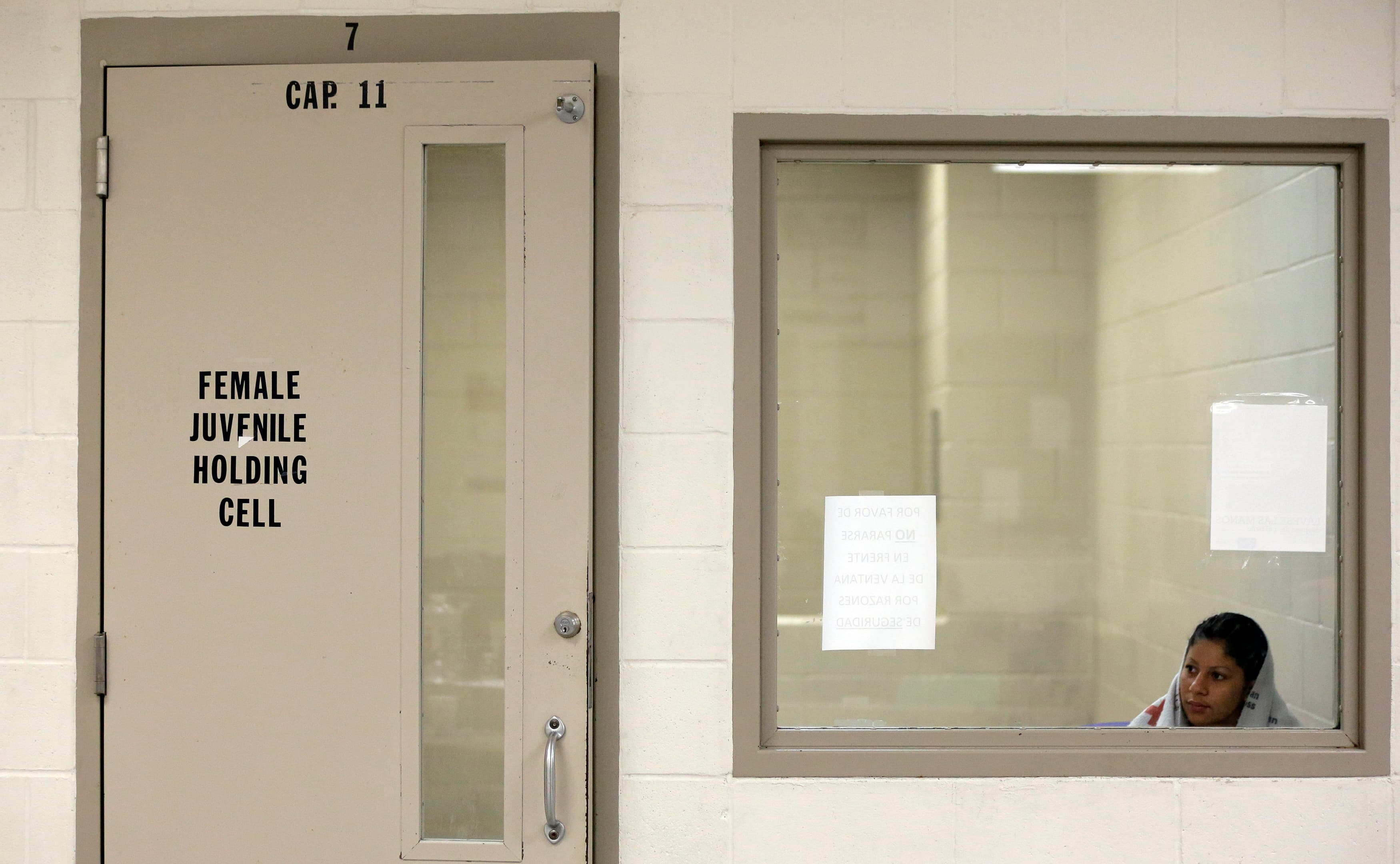 A woman looks out a window of a holding cell