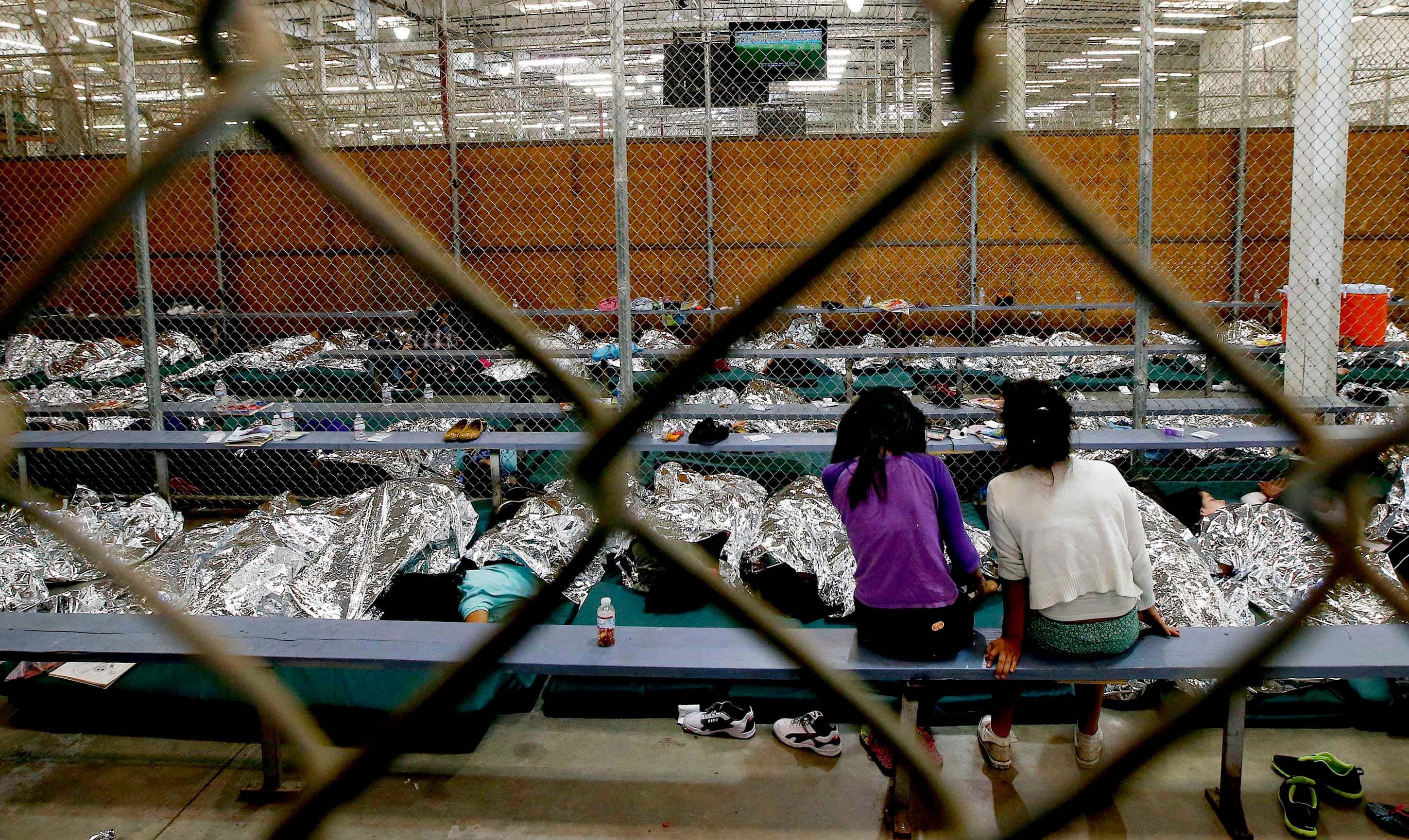 Two young girls watch television in a holding area where hundreds of mostly Central American immigrant children were being processed and held at the US Customs and Border Protection Nogales Placement Center in Nogales, Arizona, June 18, 2014.