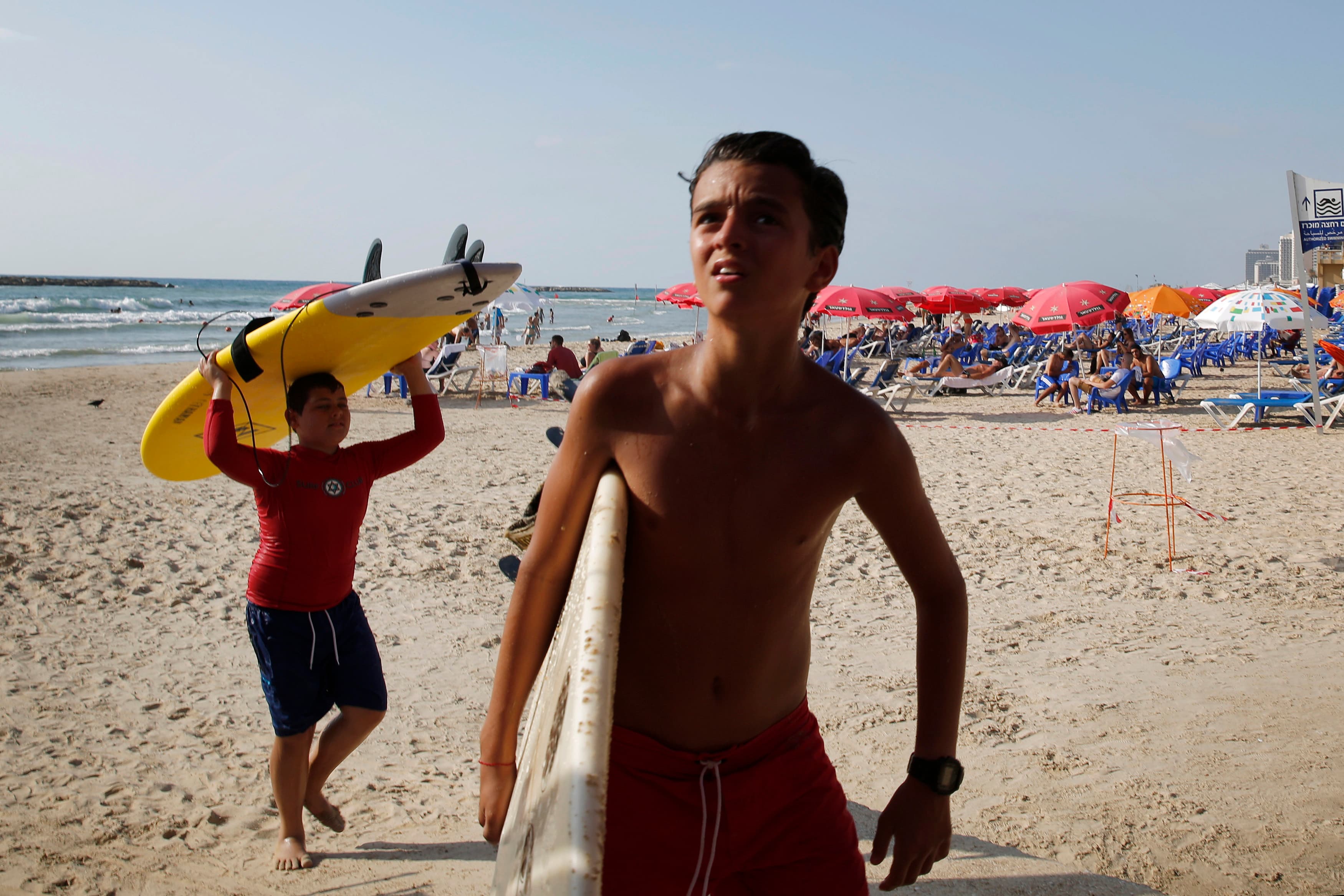 Boys carry their surfboards ashore on a Tel Aviv beach after their lesson was cancelled following a rocket from Gaza that was intercepted by Israel's Iron Dome defense system.