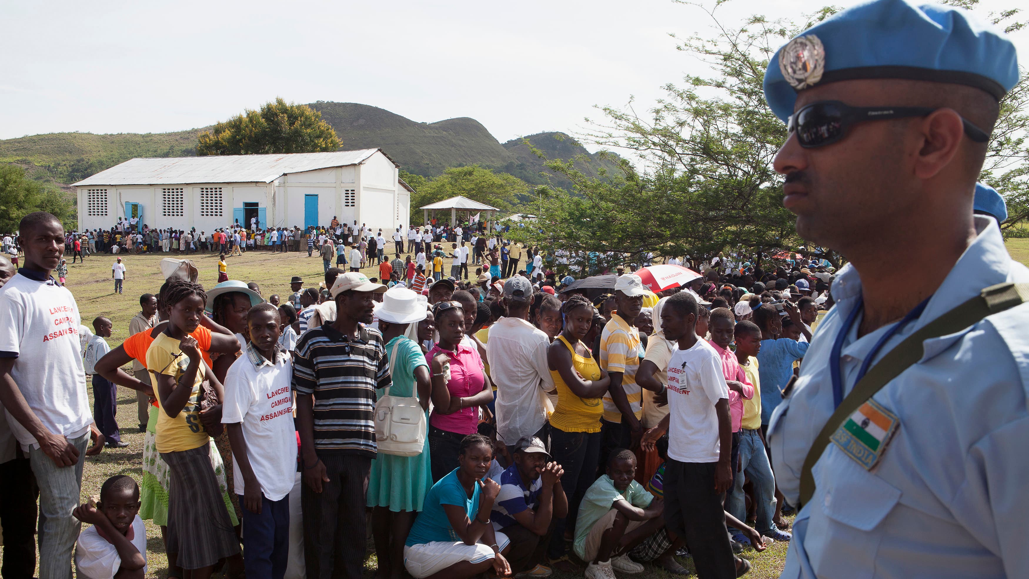 A United Nations peacekeeper stands guard are Haitians gather to see U.N. Secretary-General Ban Ki-moon visit the village of Los Palmas.