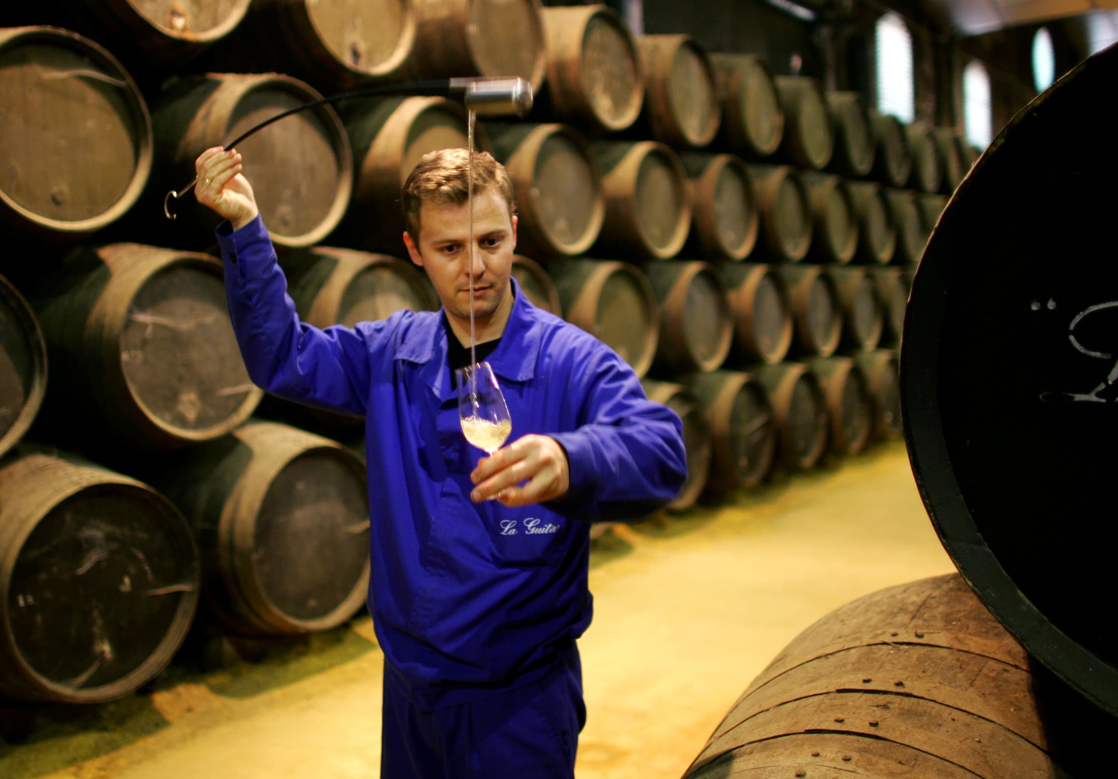A worker pours manzanilla wine into a wine taster from a oak barrel in the wine cellar "La Guita" in Sanlucar de Barrameda, southern Spain